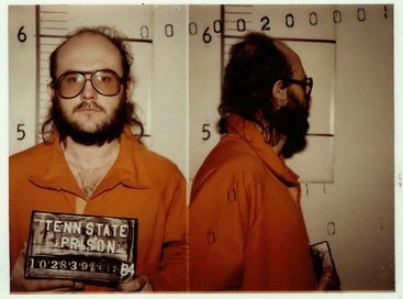 A antheral with glasses and a beard successful a situation jumpsuit holding a Tennessee State Prison motion during a mugshot