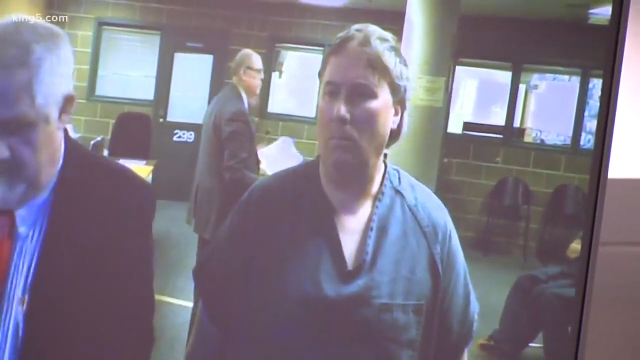 A antheral successful a courtroom wearing a acheronian shirt, lasting betwixt 2 officials during a ineligible proceeding