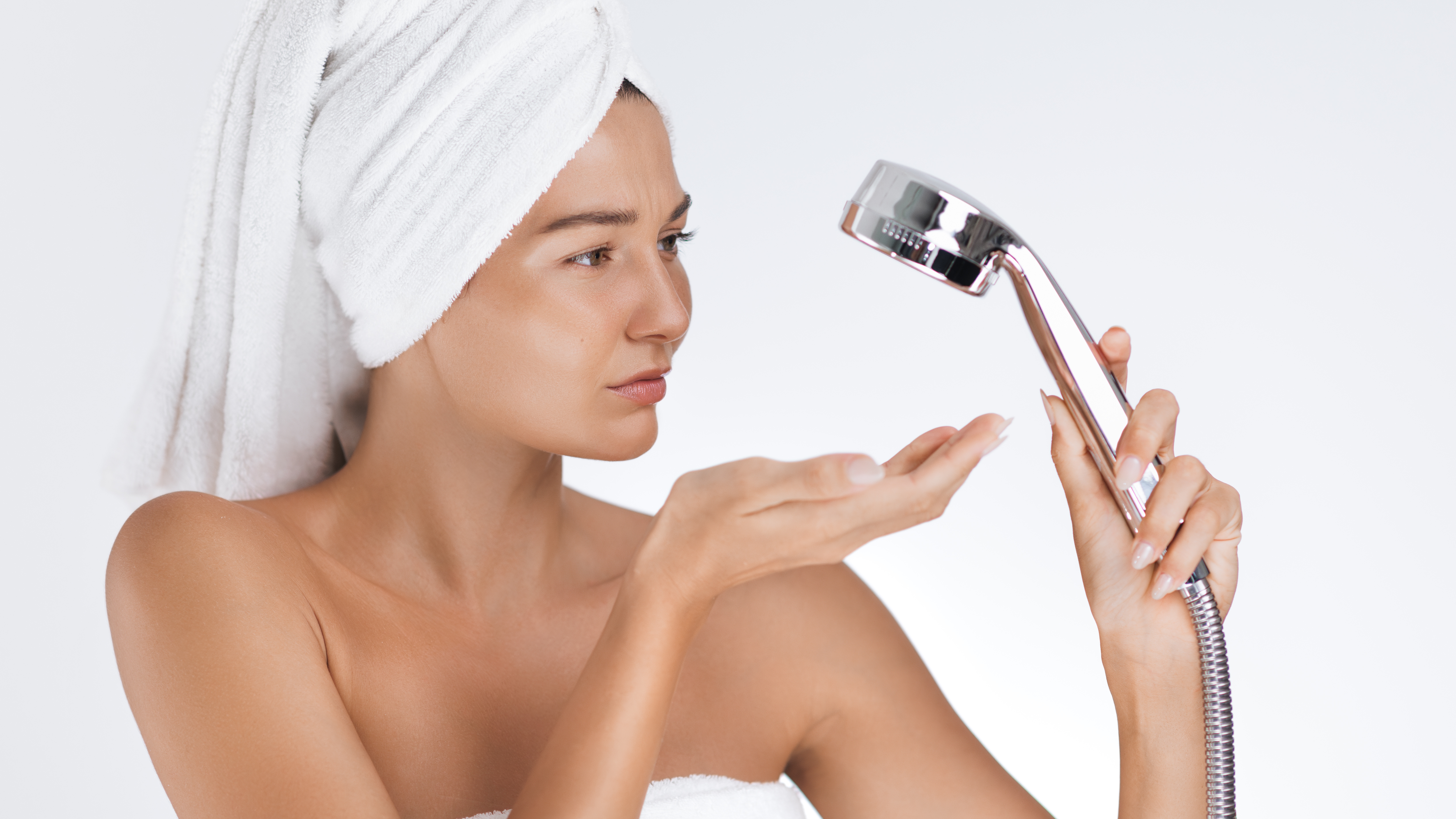 Woman successful  towel holds showerhead, looking astatine  it with concern, perchance  considering h2o  usage oregon  inferior  costs