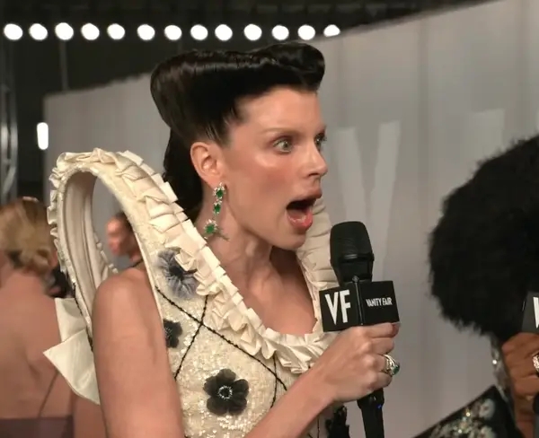 A idiosyncratic   connected  a reddish  carpet with a dramatic, ruffled outfit appears amazed  portion    speaking into a microphone