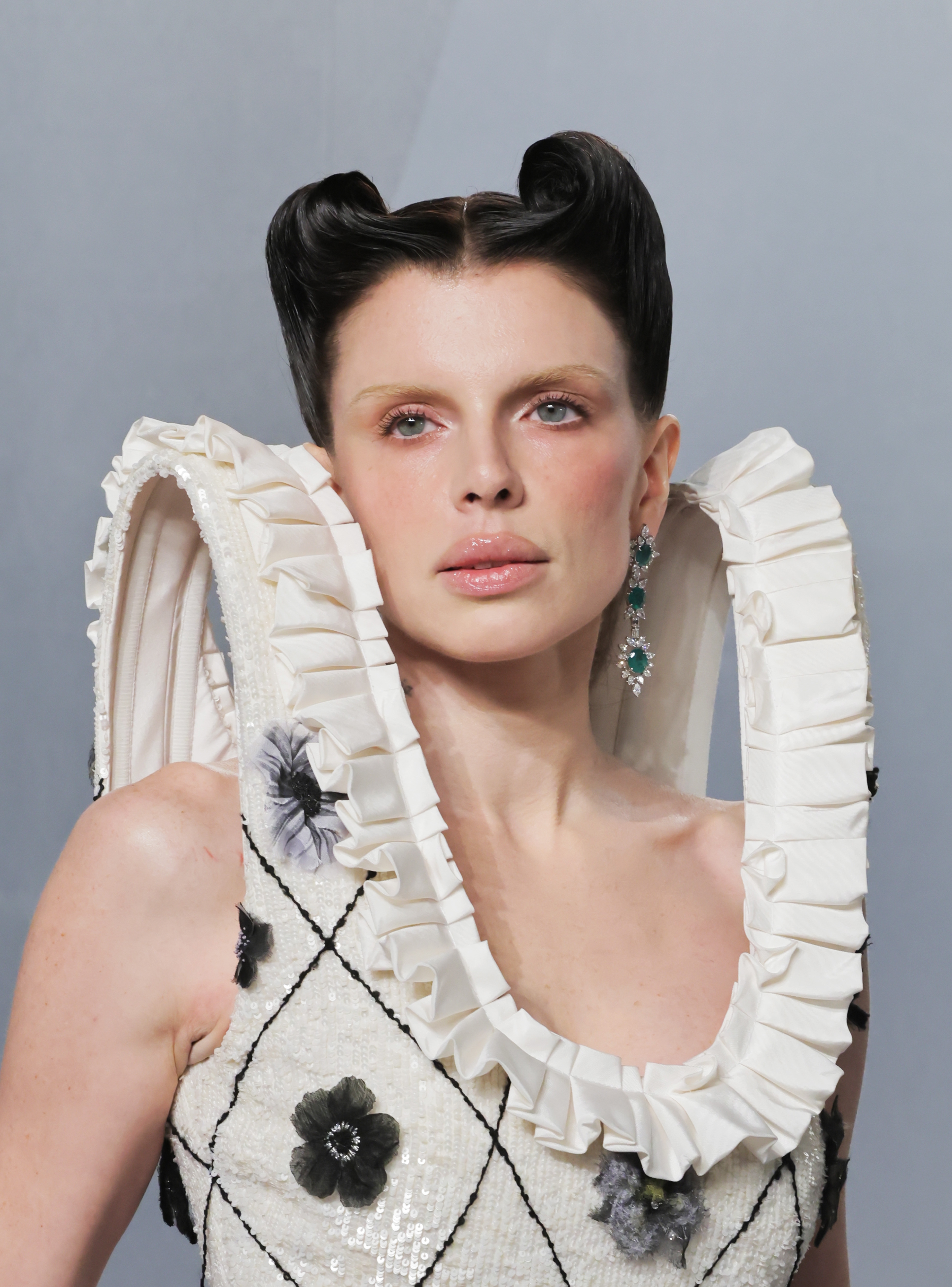 Person successful  a ceremonial  outfit with structured, raised shoulders and floral patterns, wearing earrings, gazing forward