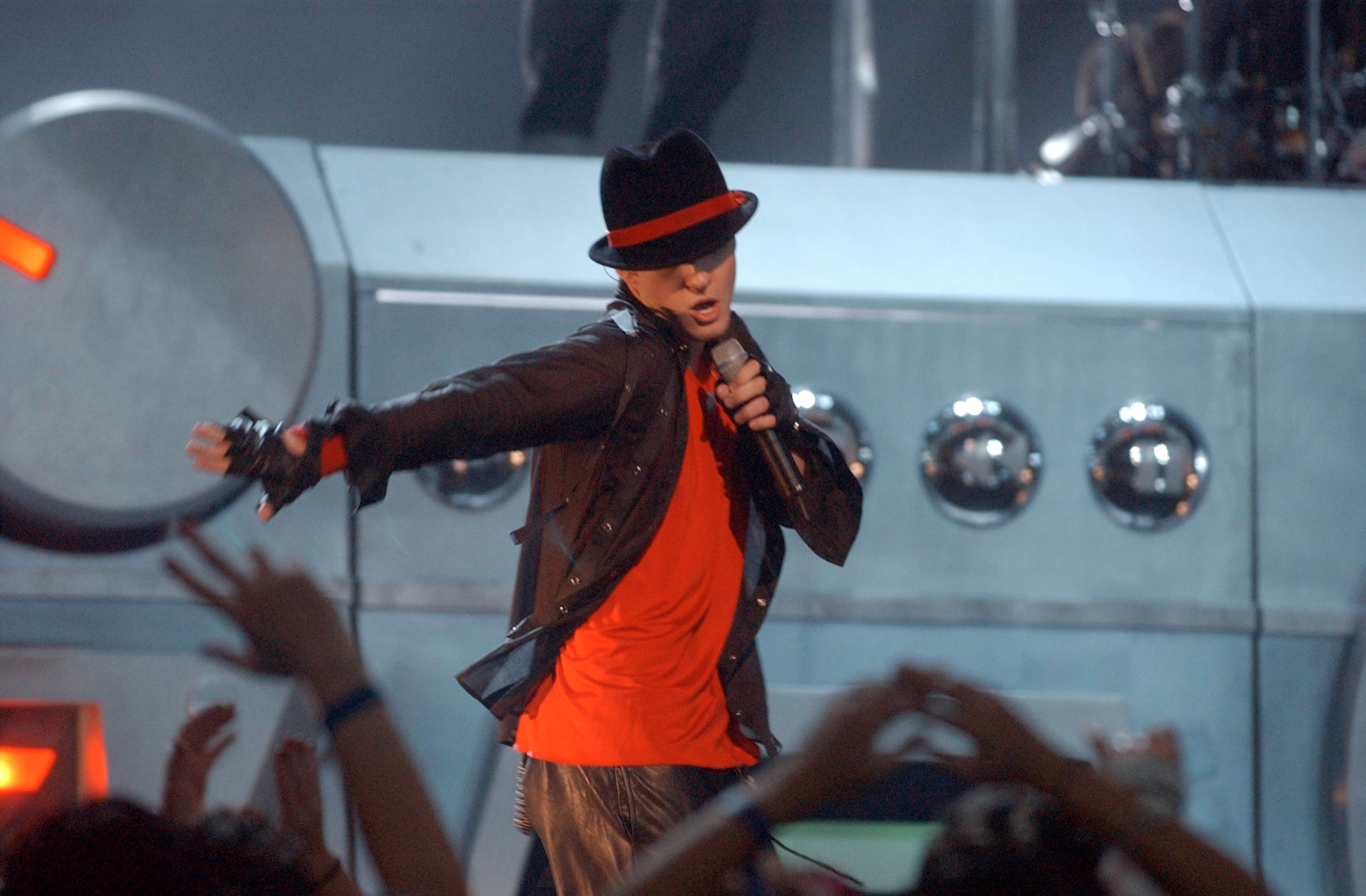 Performer connected  signifier    successful  a dynamic pose, wearing a stylish jacket, fedora, and sunglasses, holding a microphone during a concert