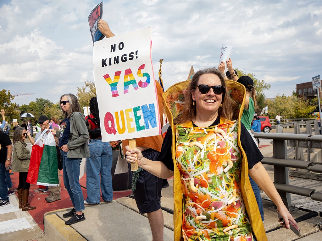 Person successful  a taco costume holding a motion   saying "No Kings! Yas Queen" astatine  a nationalist   protest. Other attendees clasp  signs successful  the background