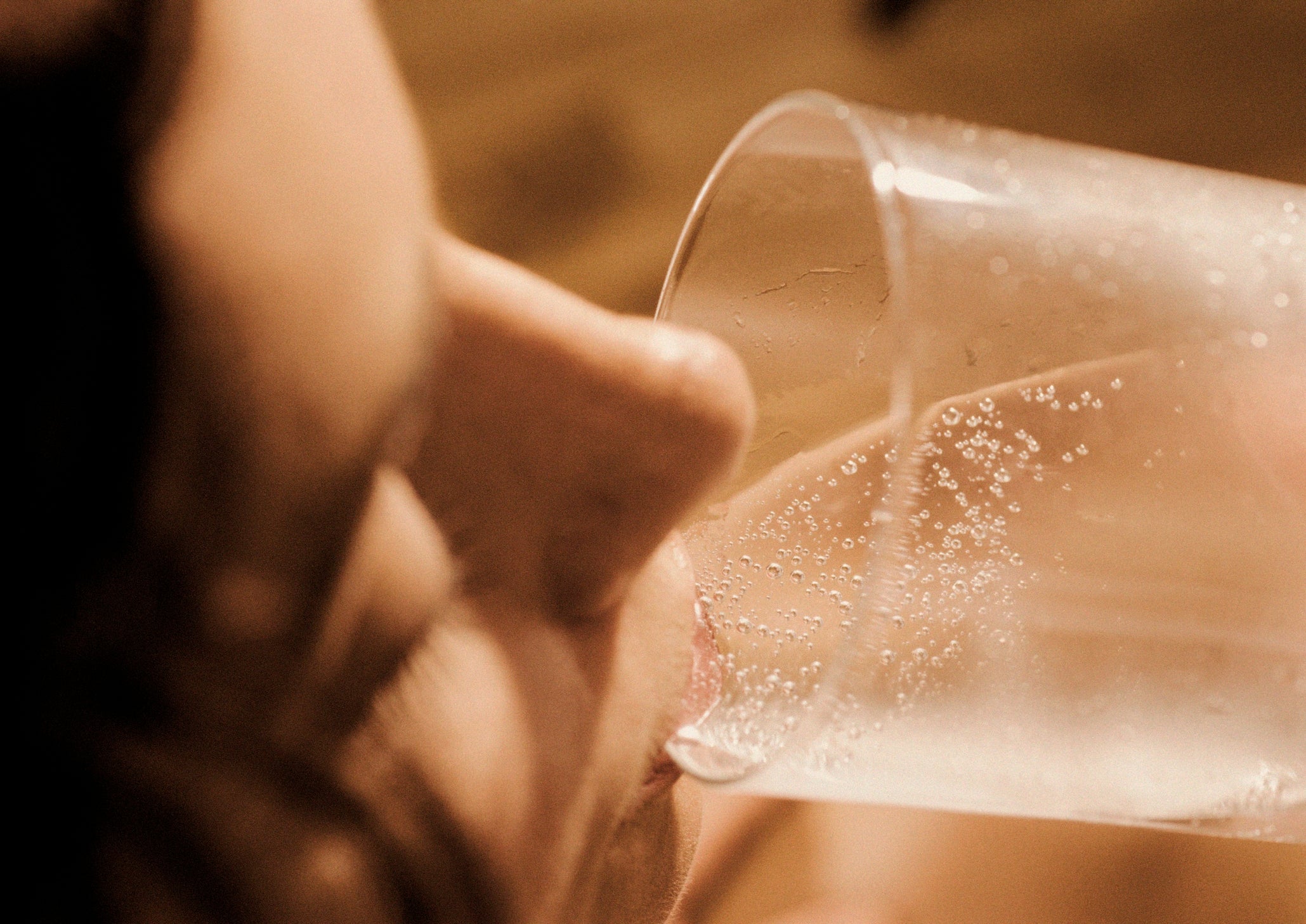 Person drinking from a clear glass with fizzy bubbles visible, suggesting a carbonated beverage. The focus is on the glass and bubbles