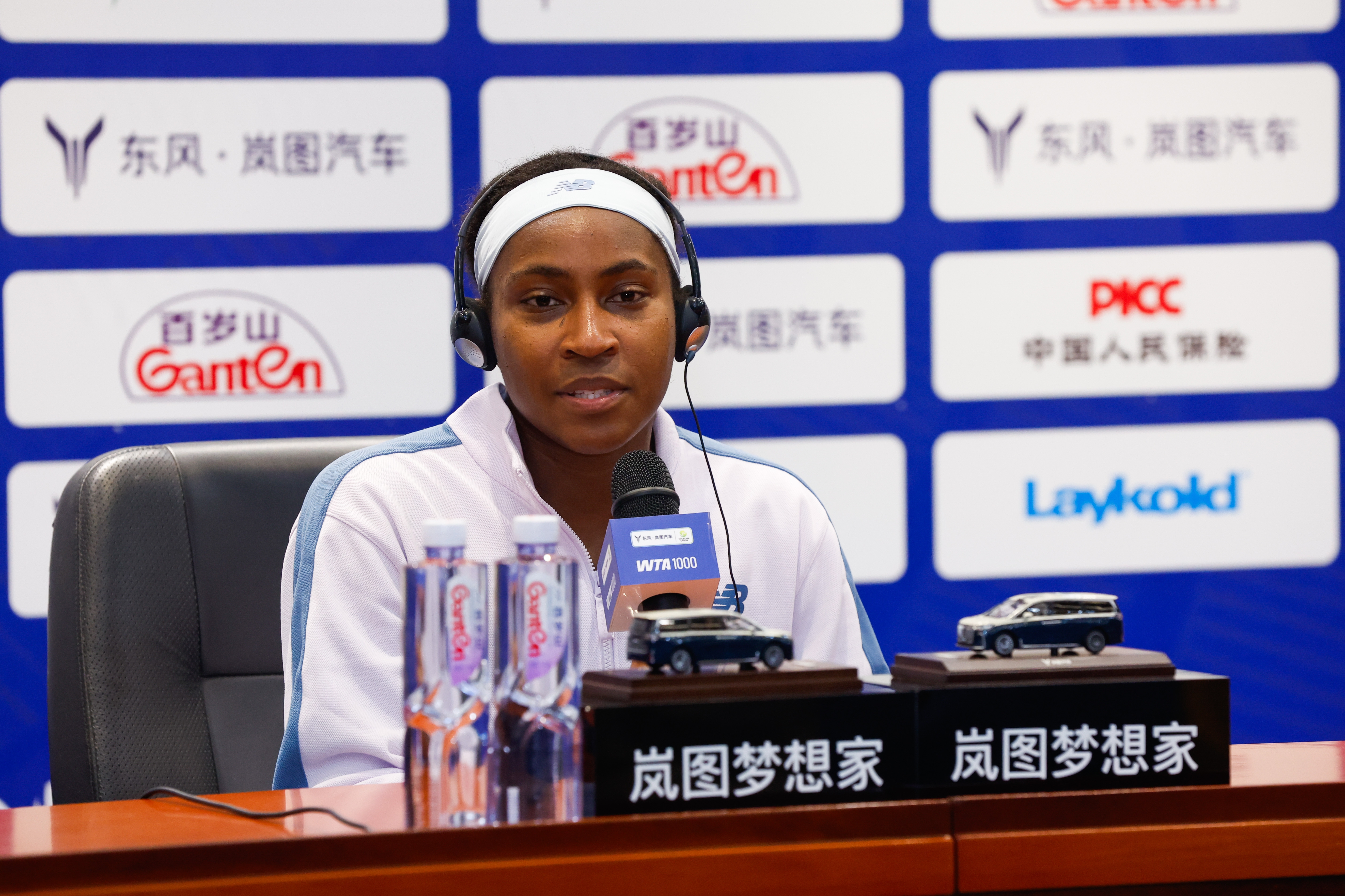 Coco Gauff speaks astatine  a property   conference, wearing a headset and a tracksuit