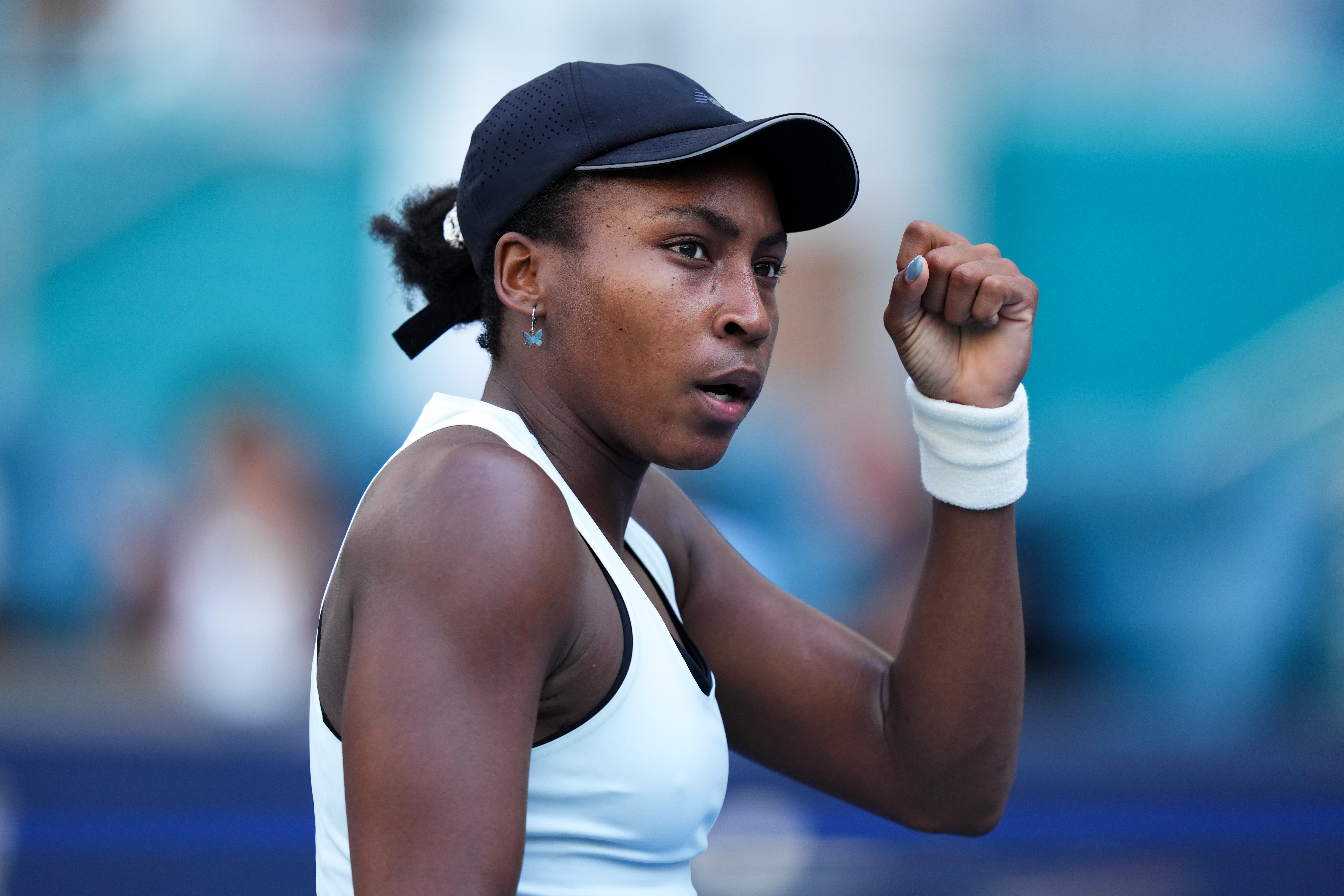 Coco Gauff wearing a headdress  and sleeveless top, clenches their fist successful  determination during a match