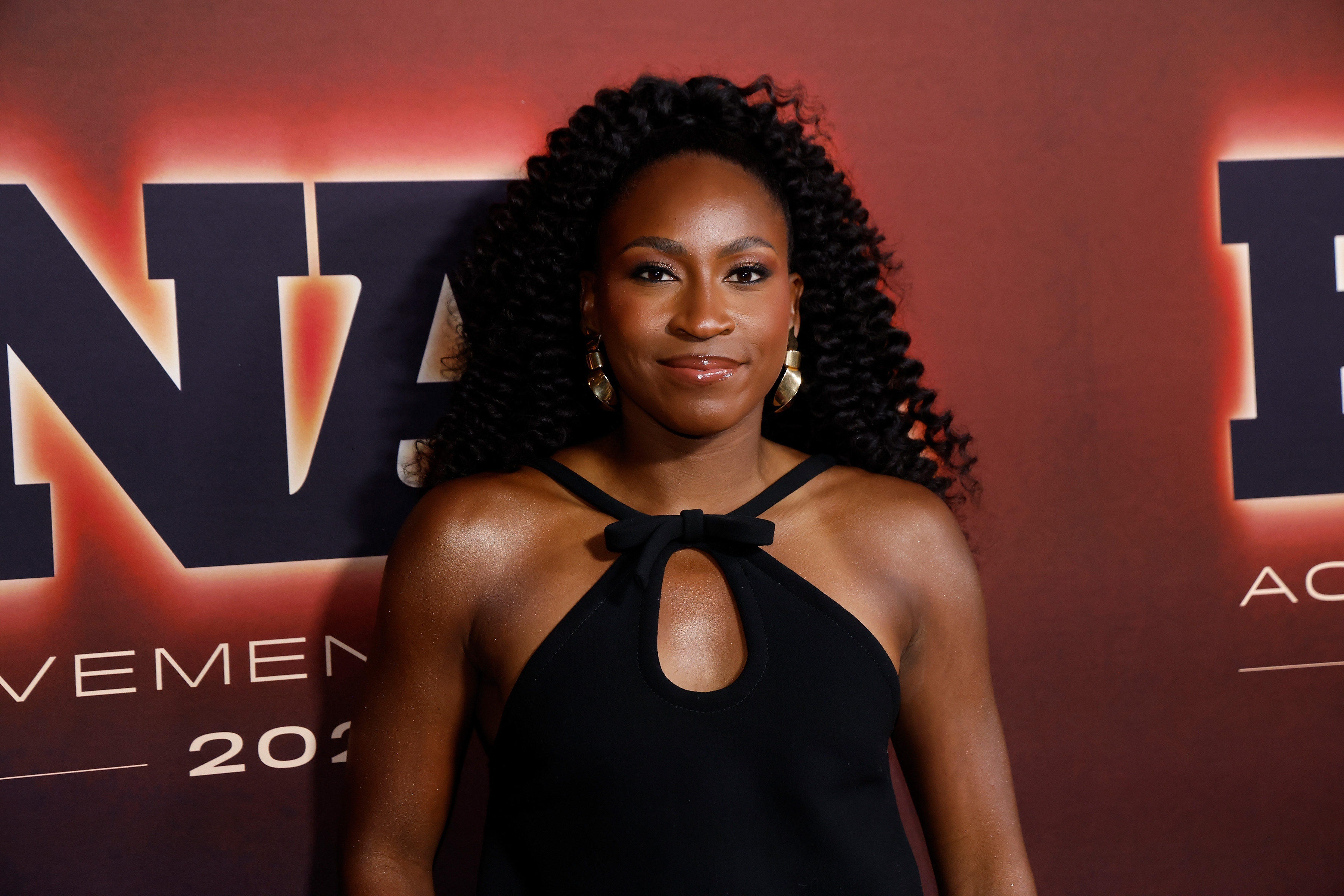 Coco Gauff posing connected  the reddish  carpet successful  a sleeveless formal  with a halter neckline and cut-out detail, with a backdrop showing text