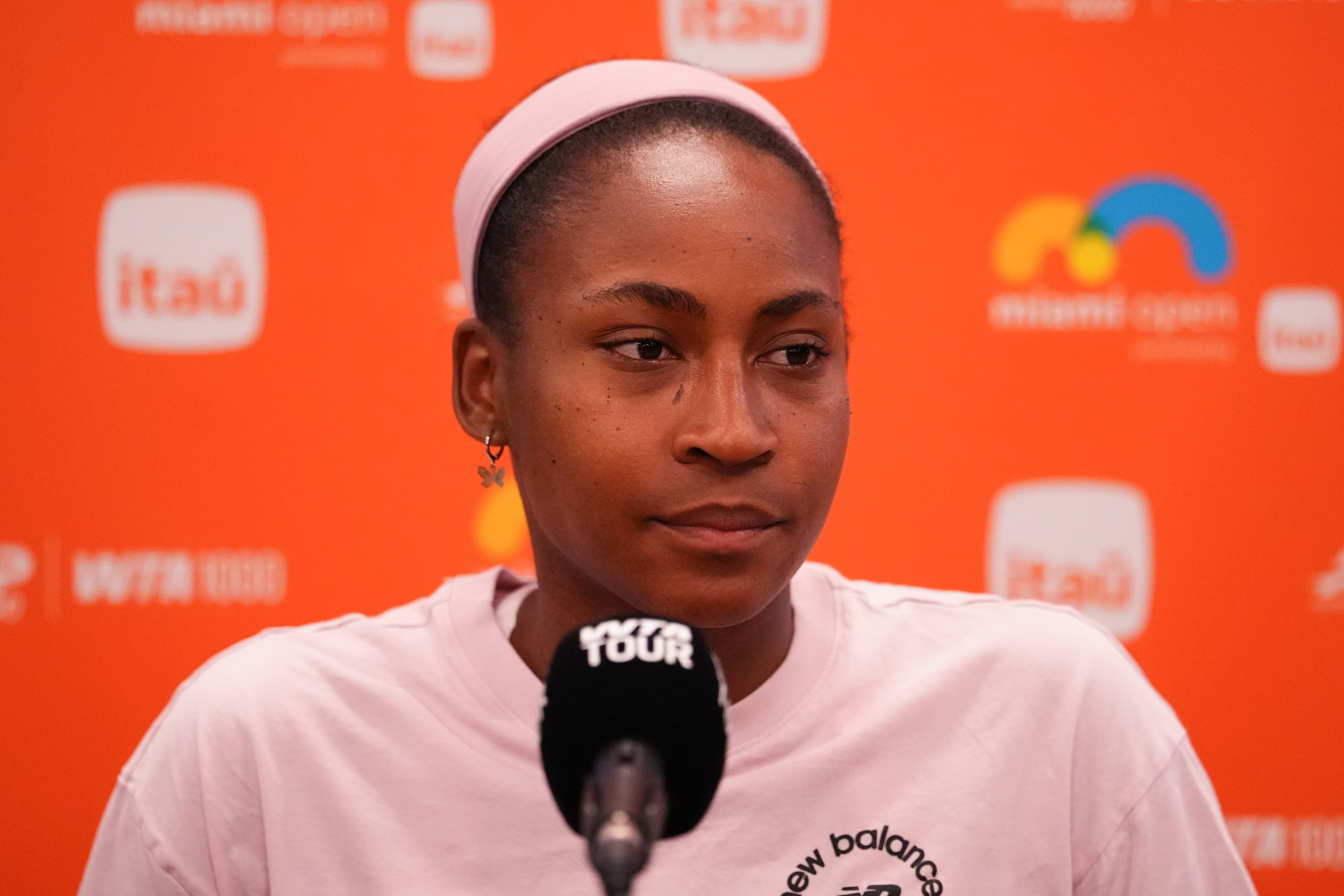 Coco Gauff astatine  a property   conference, wearing a casual t shirt, speaking into a microphone