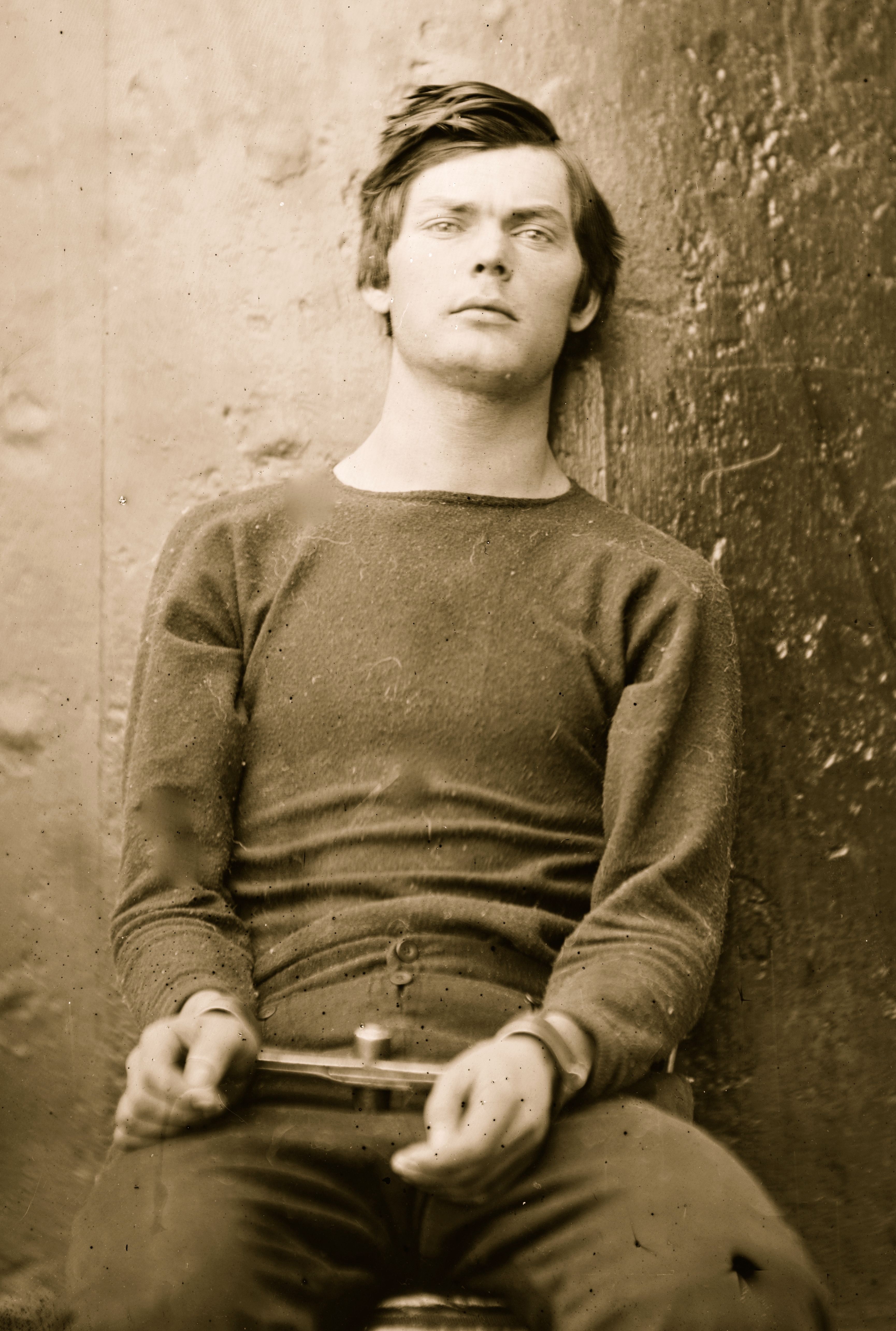 A 19th-century antheral   successful  a elemental  long-sleeved garment  holds a tiny  object, leaning against a weathered wall, gazing somewhat  upward