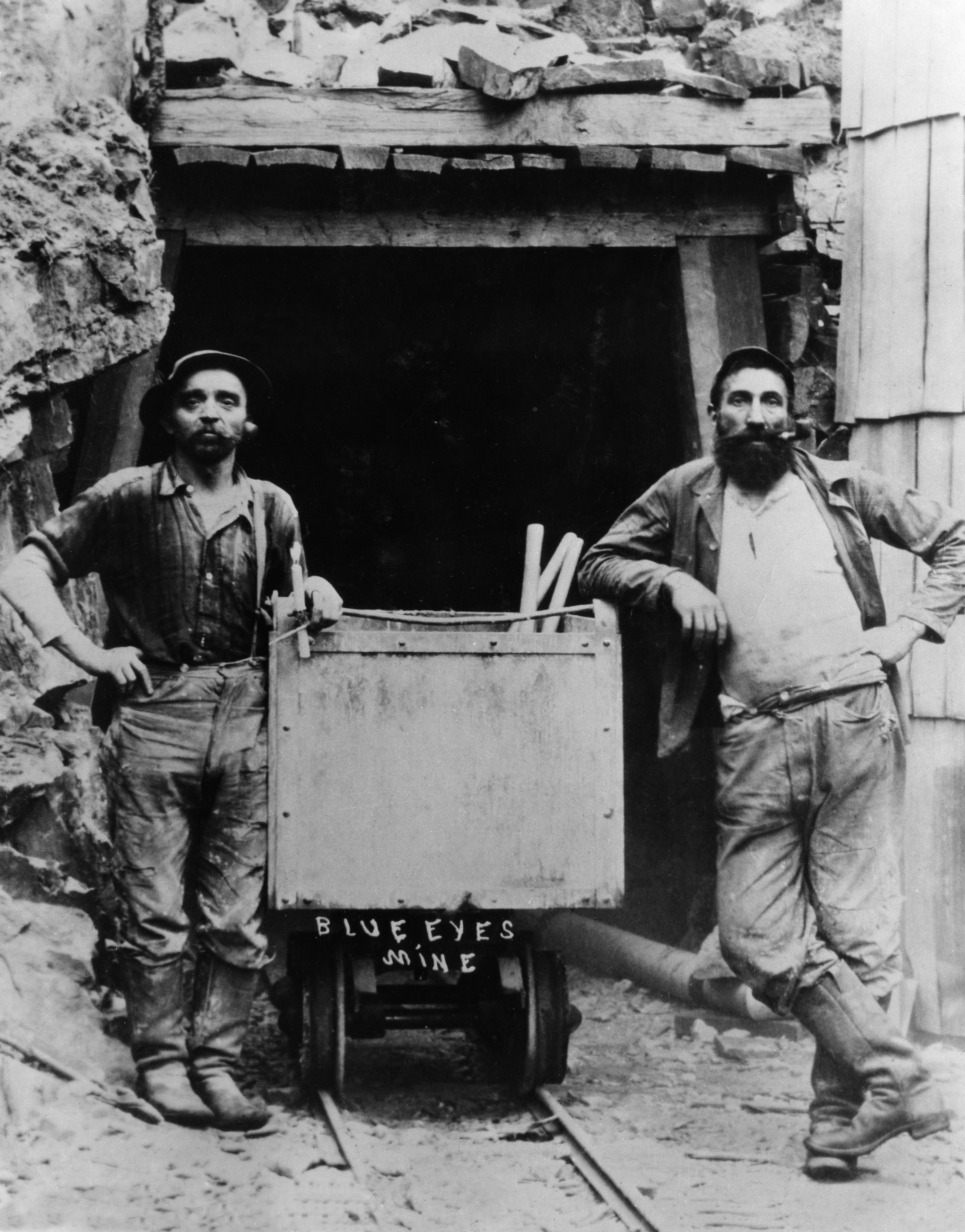 Two miners with beards and hats basal   proudly beside a mining cart labeled "Blue Eyes Mine" astatine  a excavation  entranceway  from the aboriginal  1900s