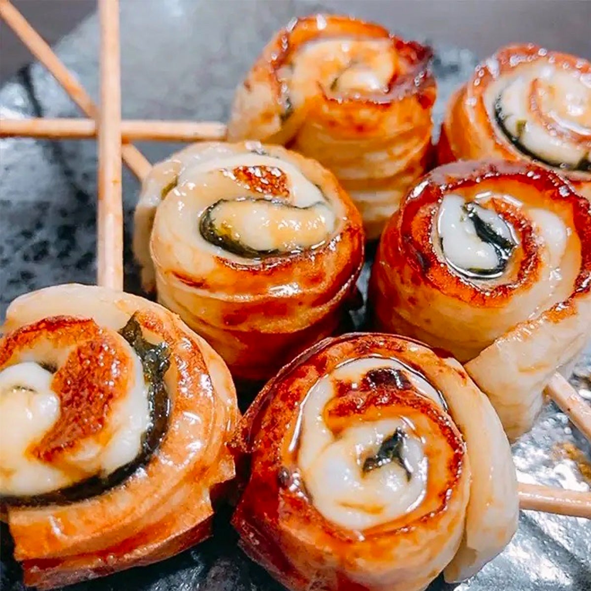 お皿に盛られた焼き鳥風串焼き。それぞれの串には渦巻き状の肉が刺さっている。