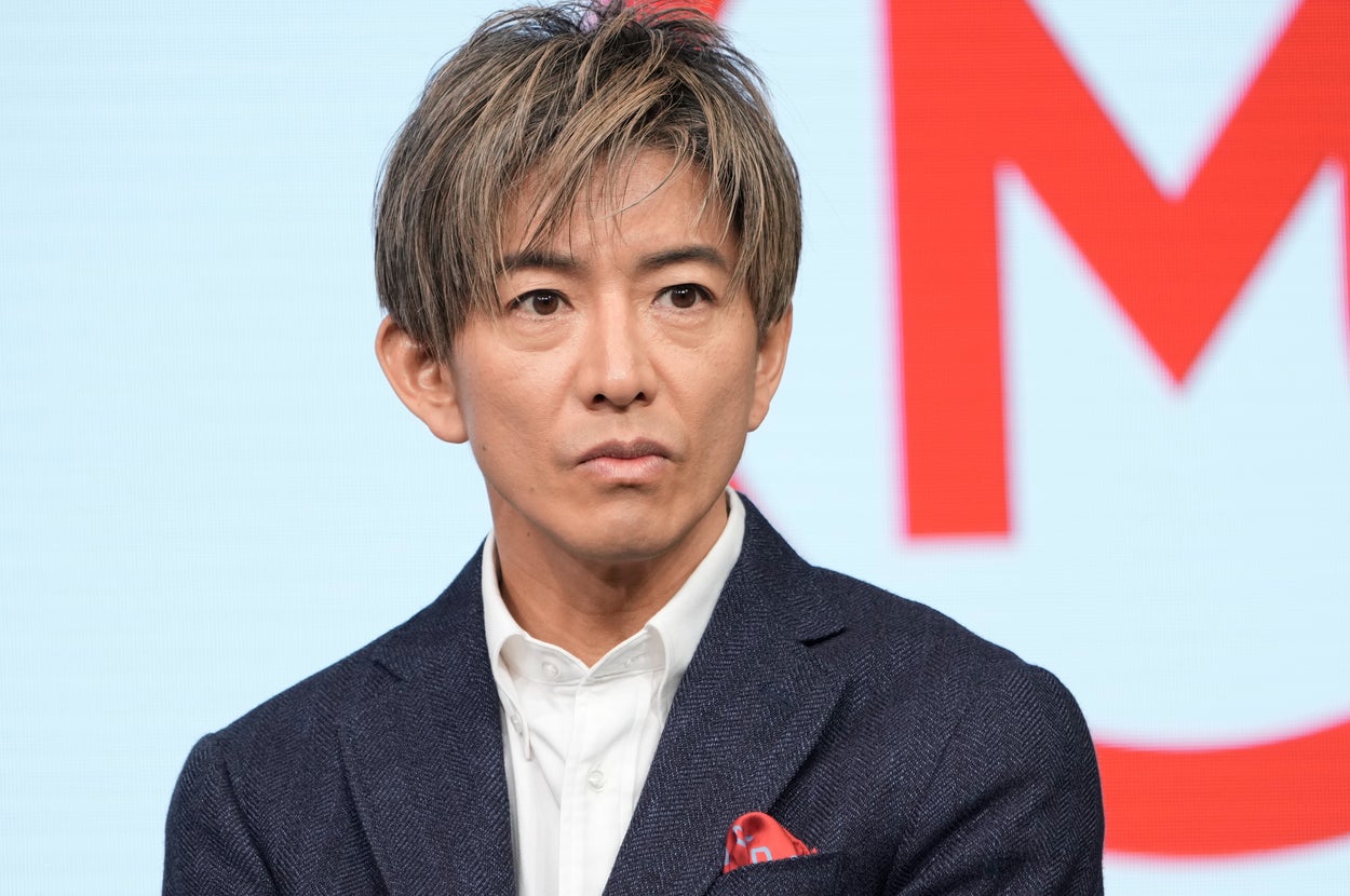 男性がフォーマルなスーツ姿でインタビューに答えている様子。背景に赤い文字。