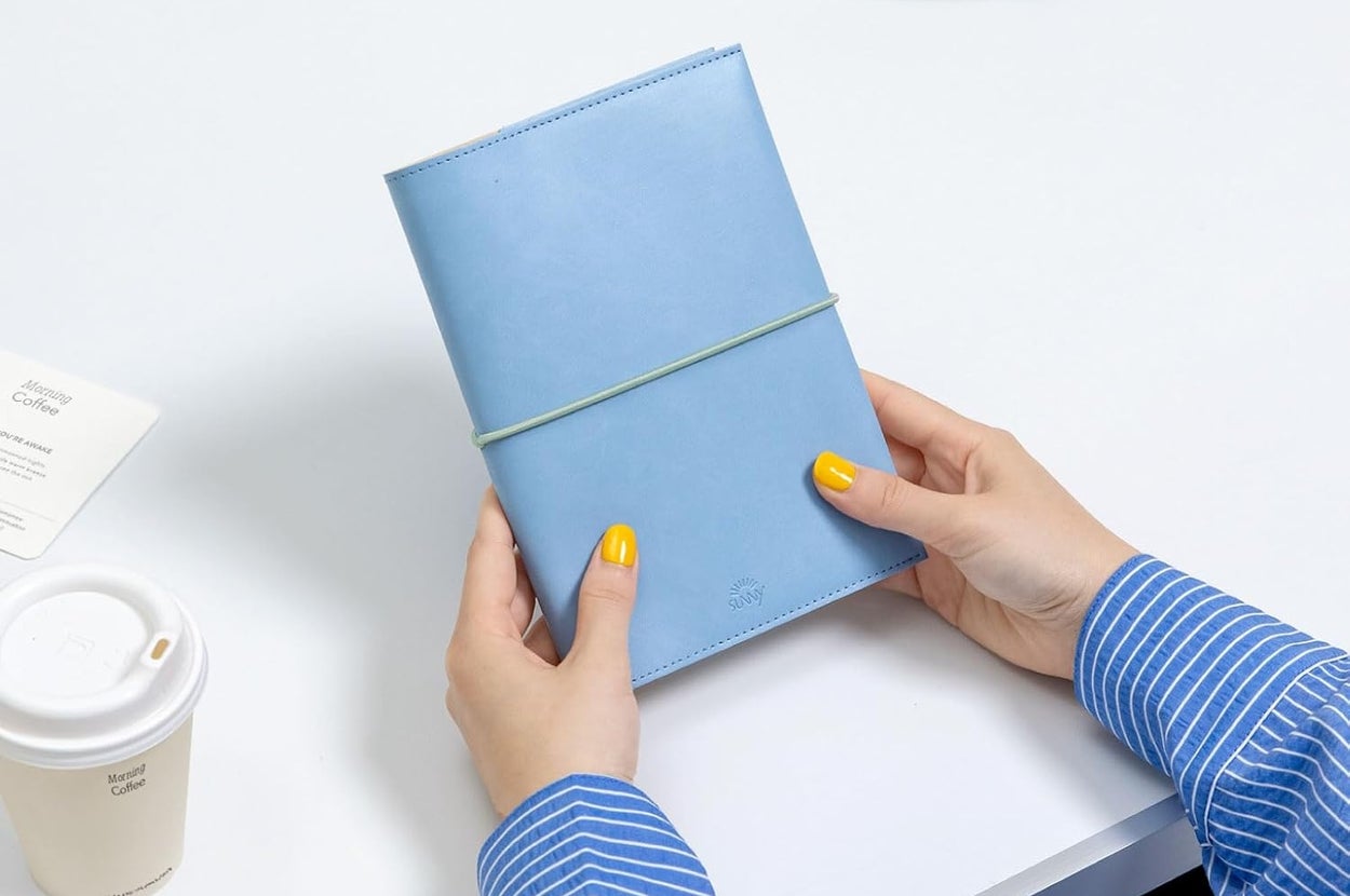 青い手帳を持つ人とカフェテーブル。コーヒーカップとクロワッサンがある。