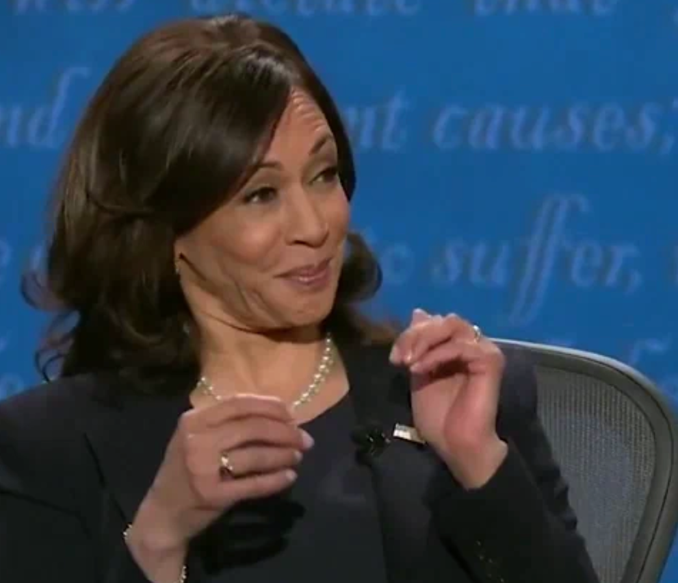 Person som smiler under en debatt, iført blazer og perlekjede, med gestikulerende hender