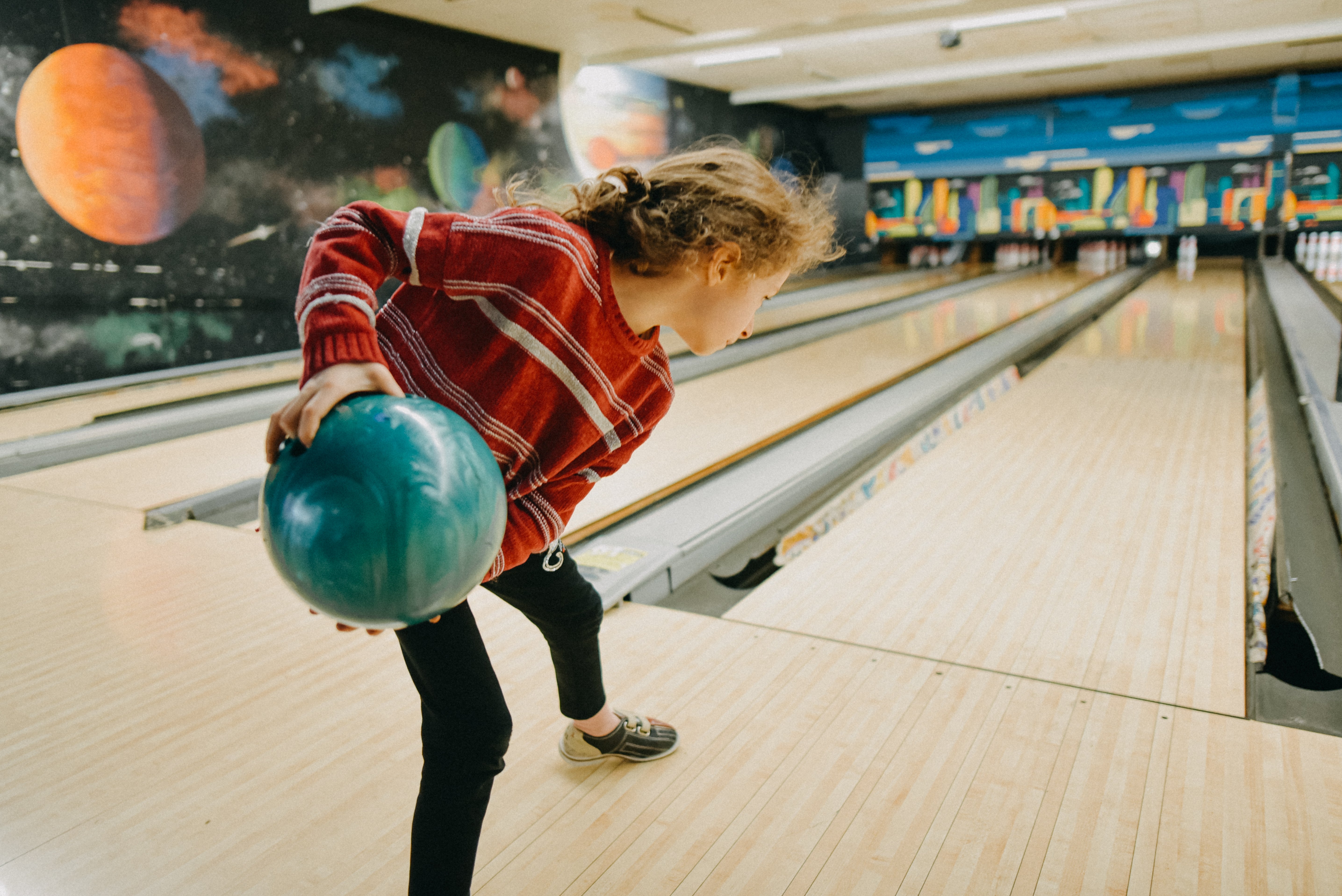 Person bowling astatine  an alley with space-themed decor, focused and mid-swing, holding a bowling ball