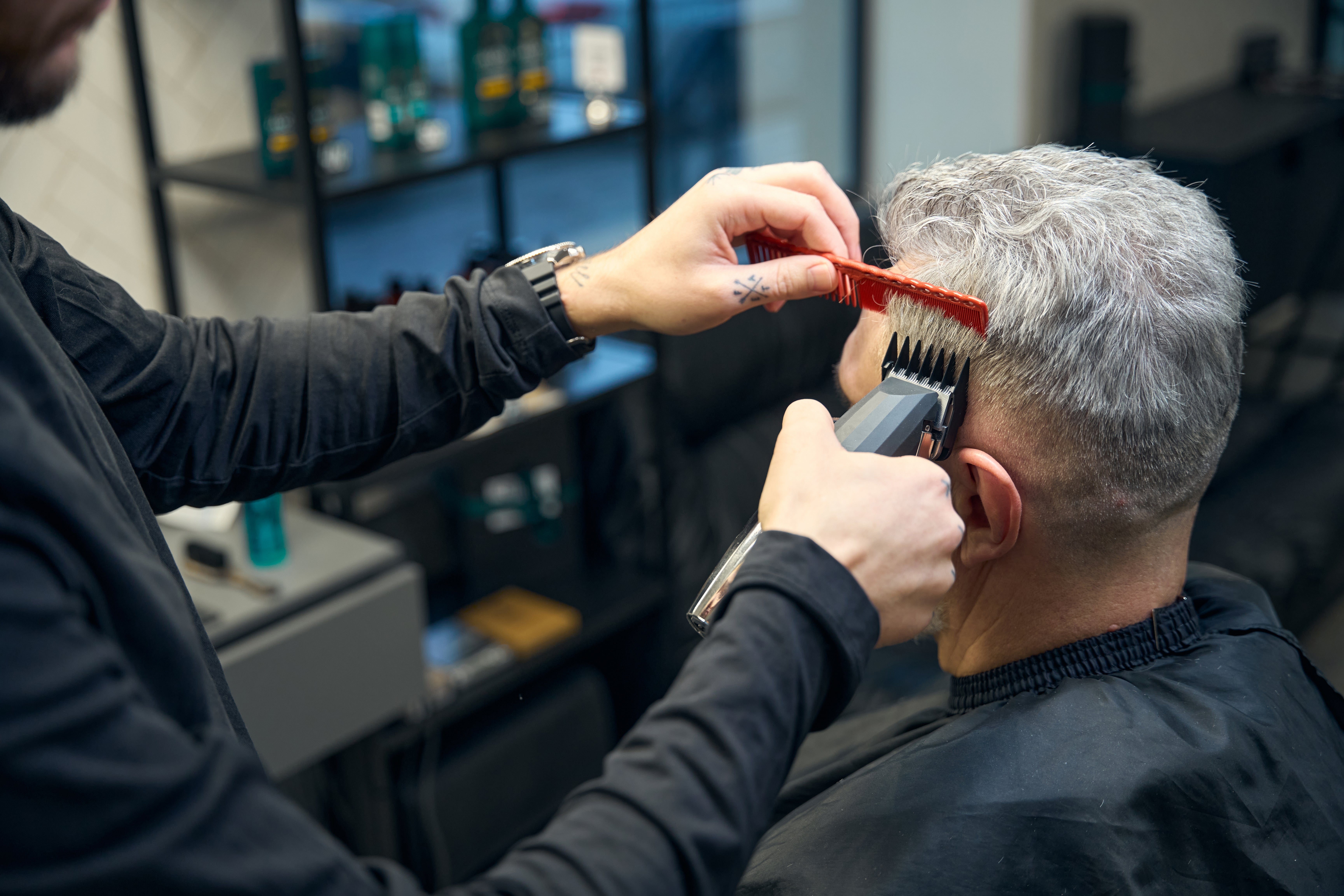 A idiosyncratic   successful  a salon gets a haircut with clippers and a comb. Shelves with hairsbreadth  products are disposable   successful  the background
