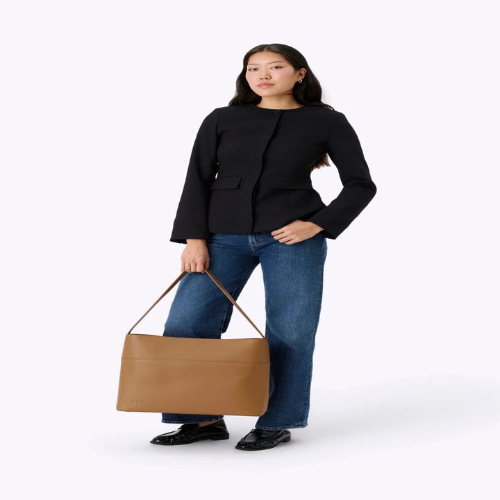 Person posing with a stylish black jacket, wide-leg jeans, and carrying a large tan handbag, suitable for a shopping feature