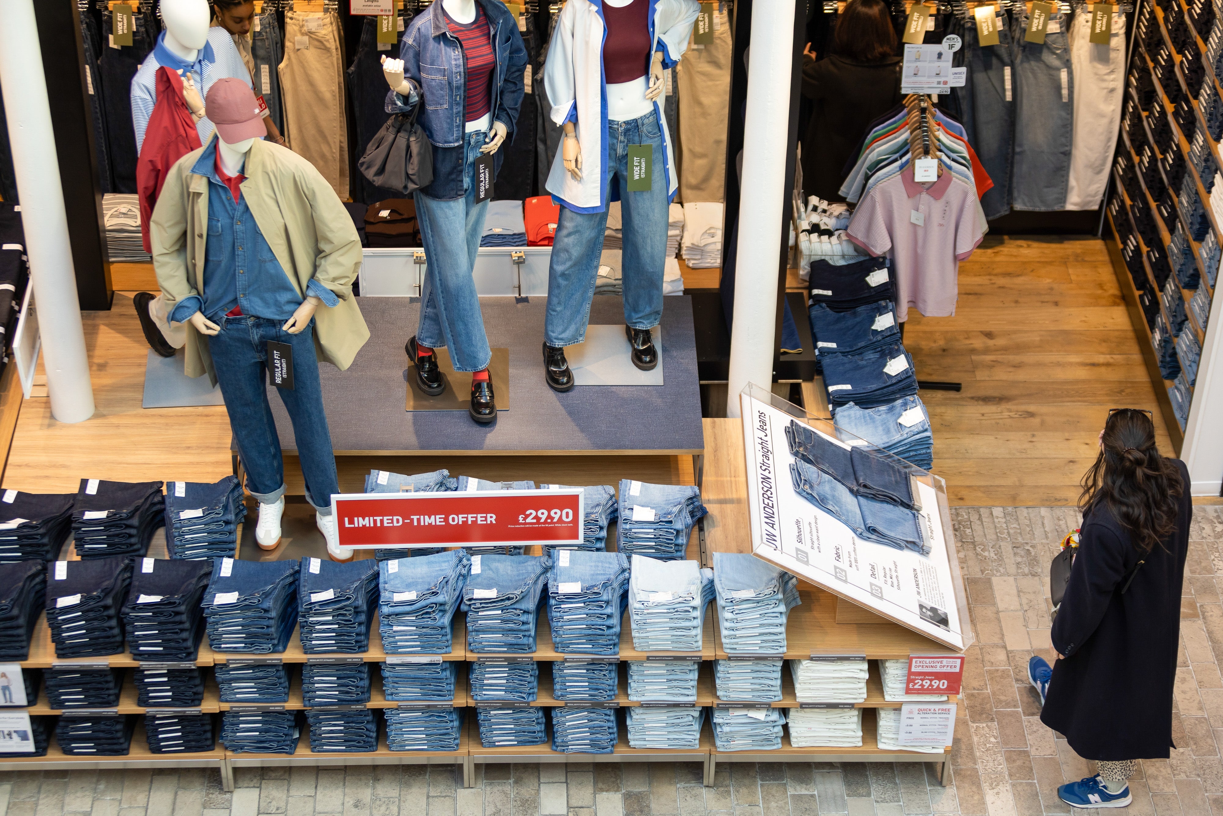 Clothing store   displaying mannequins successful  casual outfits and stacks of folded jeans. "Limited-time offer" motion   visible. Customer browsing