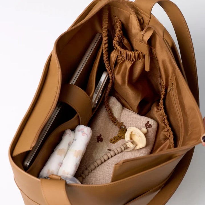 Open leather tote with a laptop, baby accessories, and a pair of rolled-up clothing inside