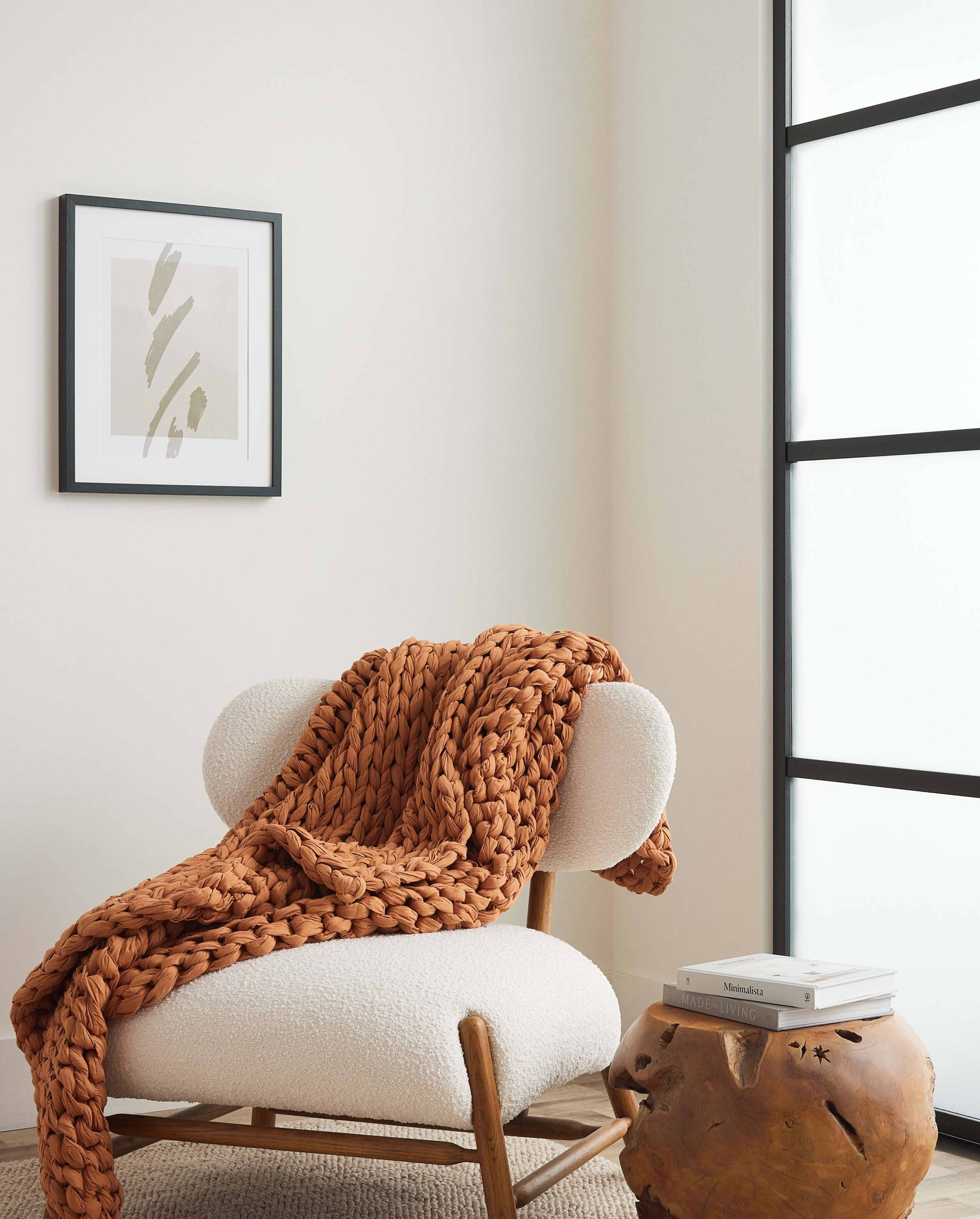 Modern minimalist living room with a white cushioned chair, a chunky knit blanket, and a side table with decor items