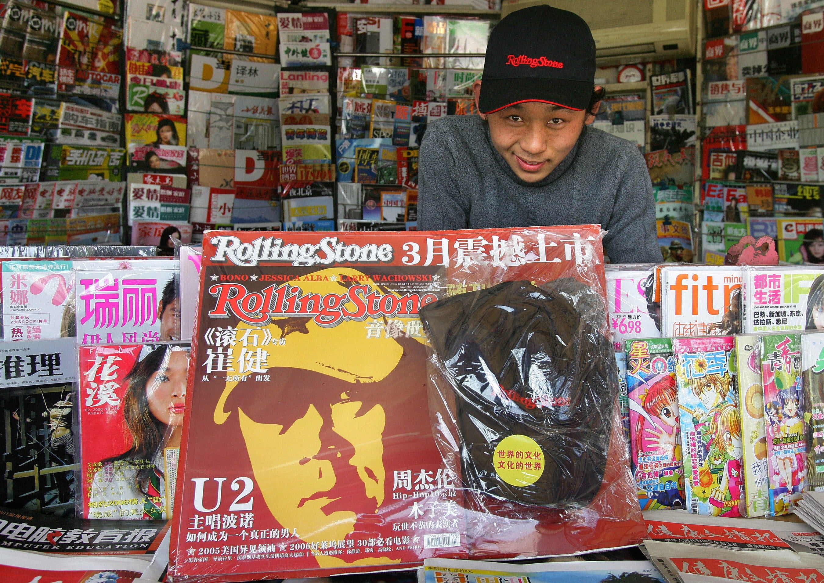 Newsstand vendor with a assortment  of magazines, including a salient  "Rolling Stone" screen  featuring U2