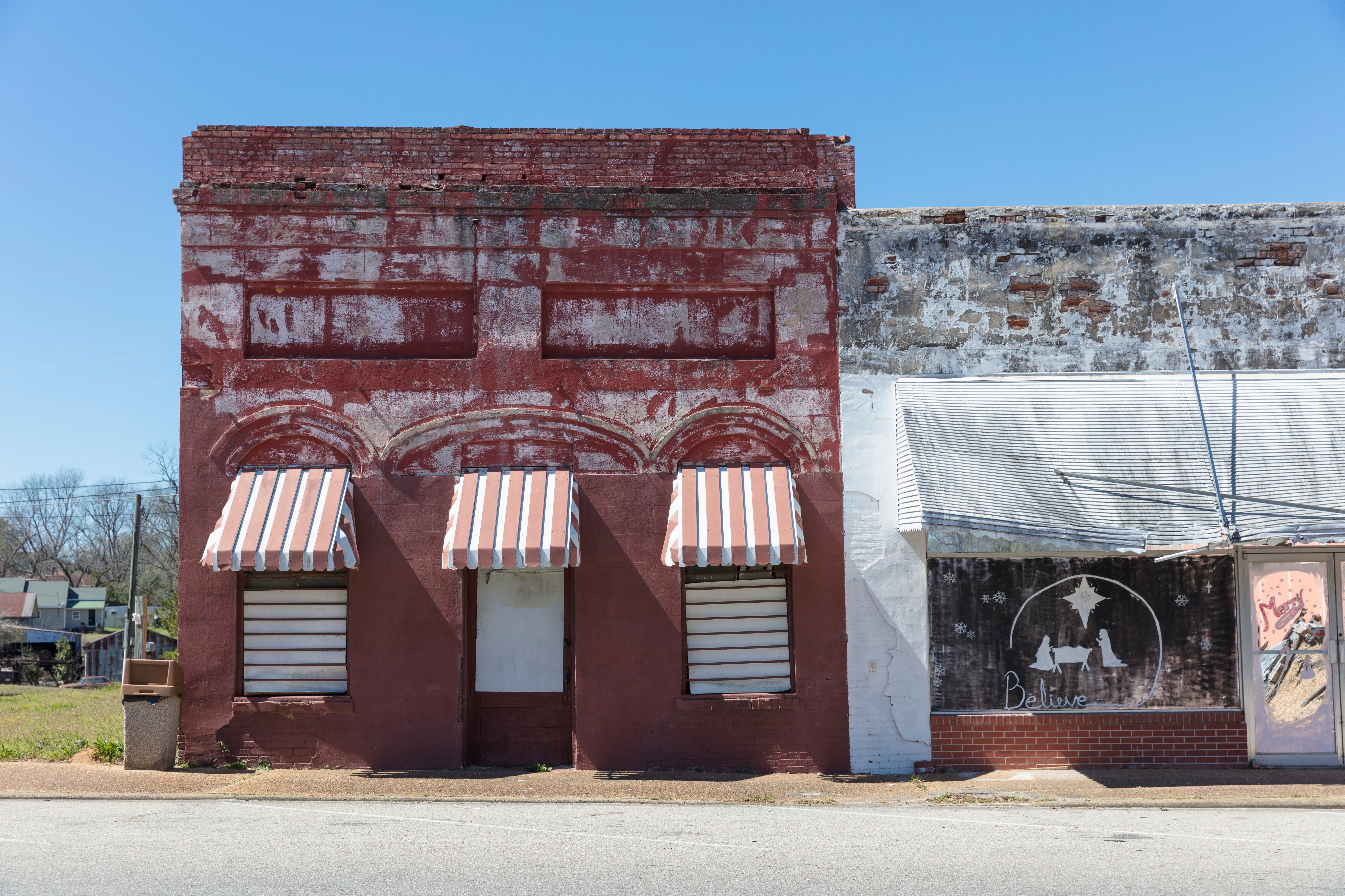 Facade of an abandoned ceramic  gathering  with striped awnings, alongside a worn mural of a canine  connected  a neighboring shop. Rural, nostalgic setting