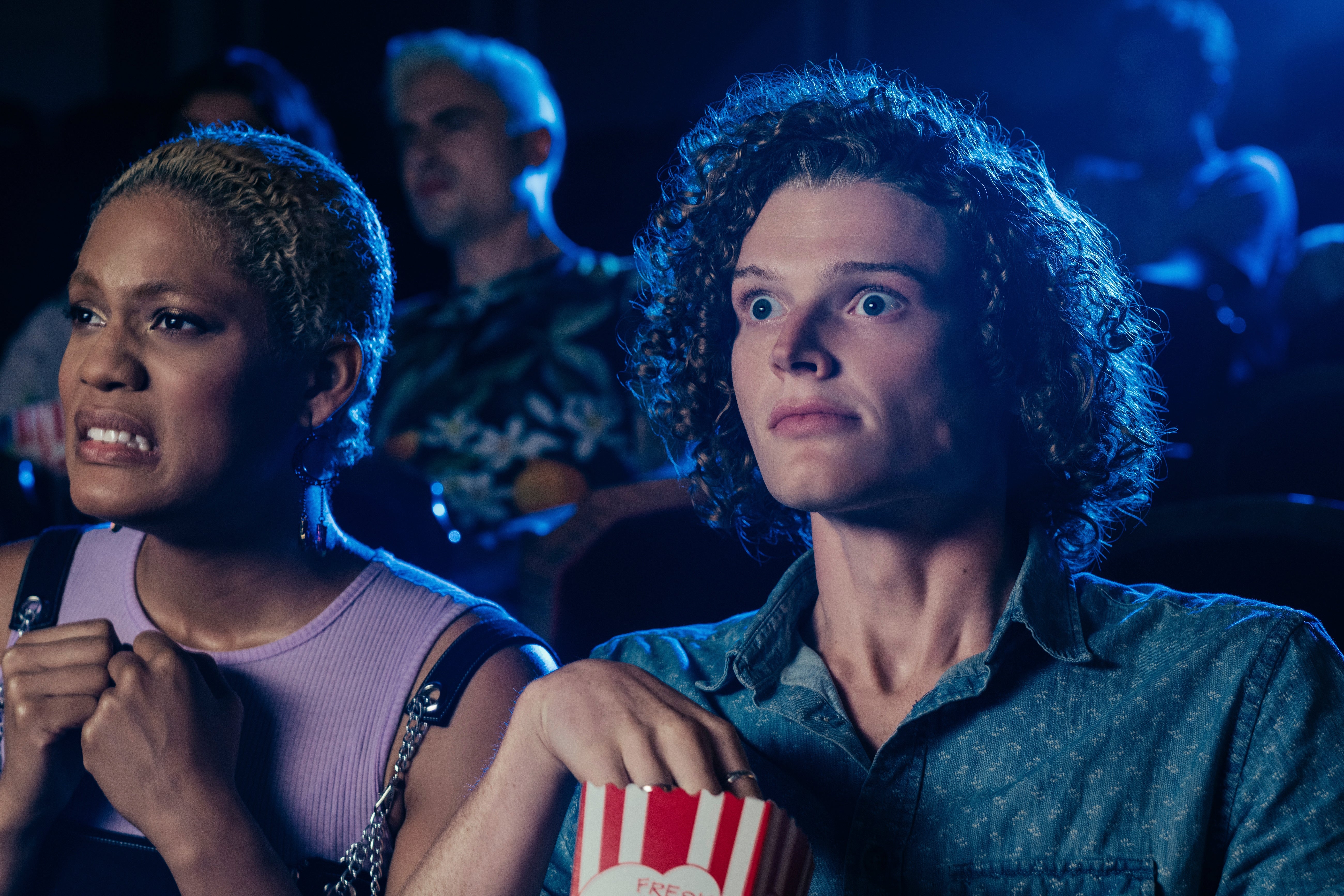 Two radical   successful  a theater, looking intensely astatine  the screen. One idiosyncratic   clutches their seat, and the different   holds popcorn, some  appearing captivated