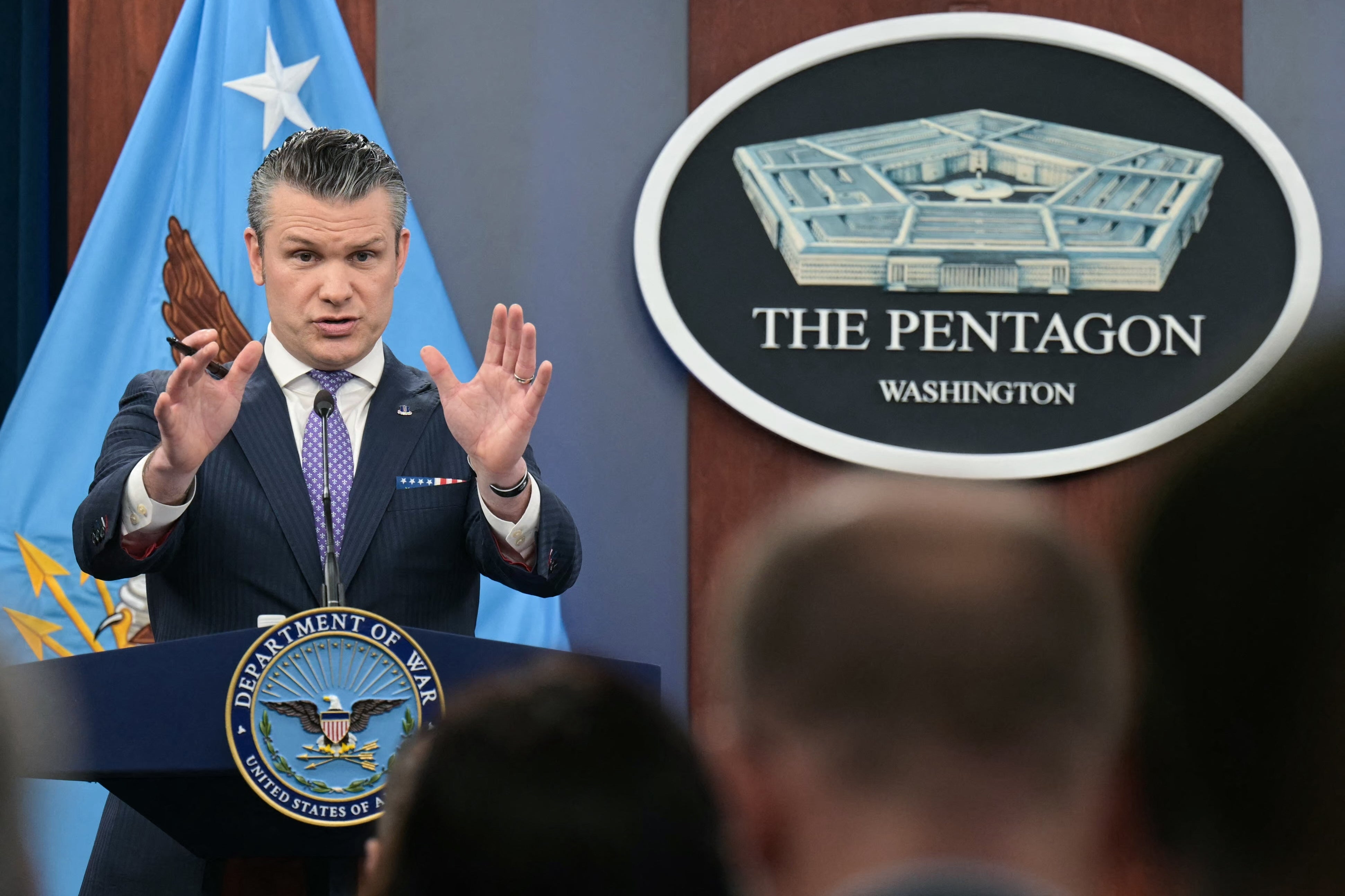 En person snakker på et podium med et Pentagon-skilt i bakgrunnen, og gestikulerer med begge hender under en pressebegivenhet