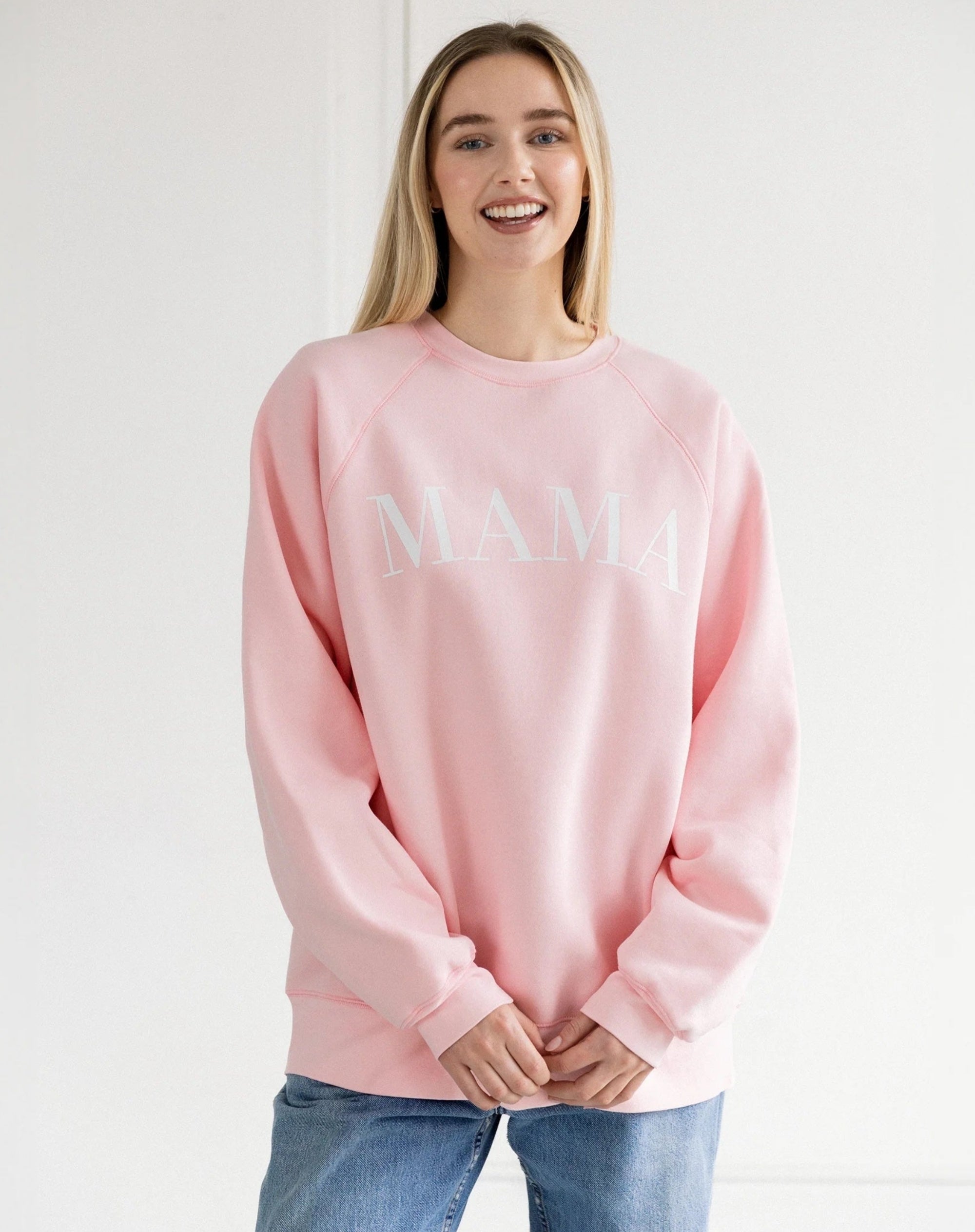 Person wearing a casual "MAMA" sweatshirt and jeans, standing and smiling