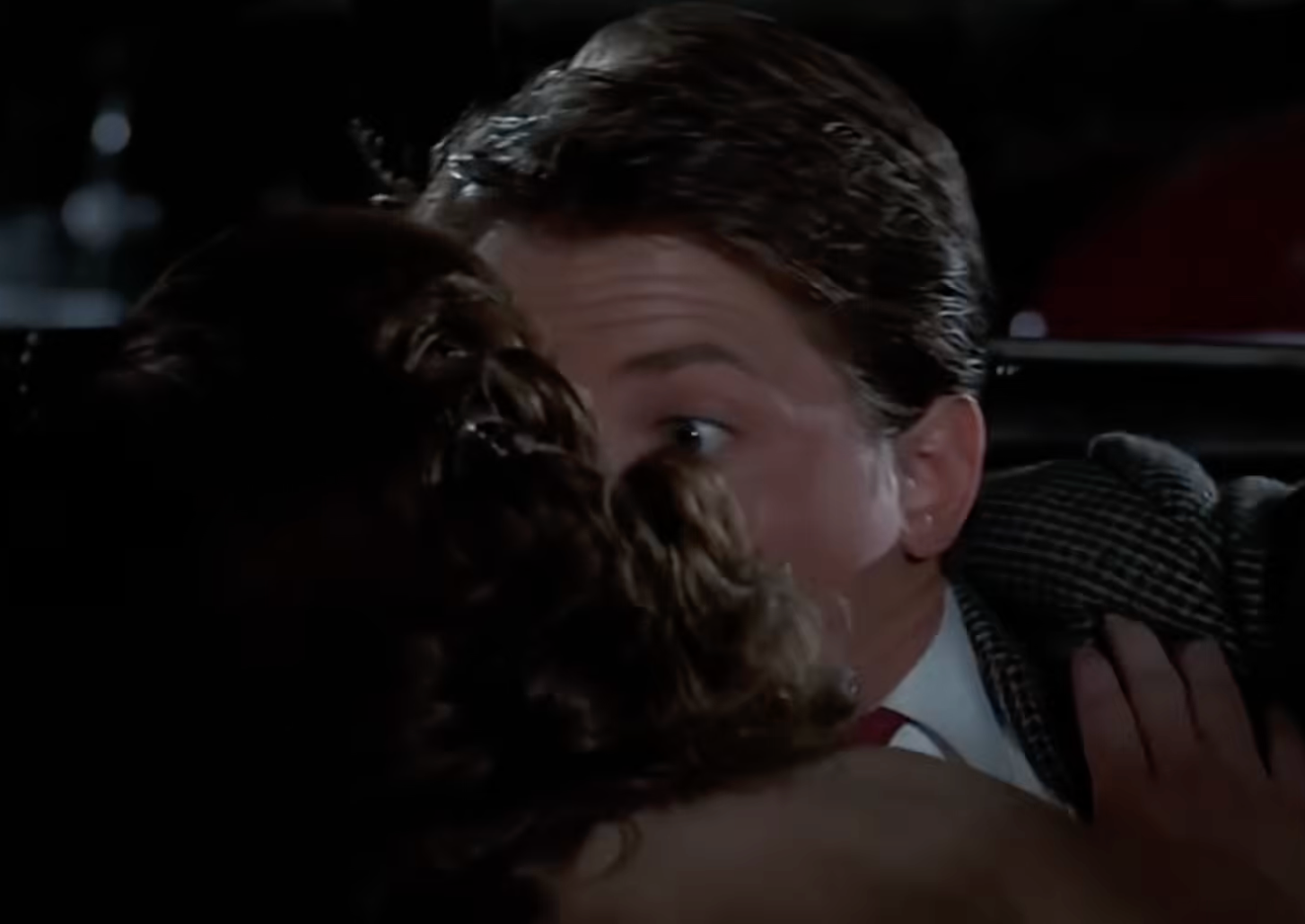 A amazed antheral successful a suit looks wide-eyed portion being kissed by a idiosyncratic with curly hair