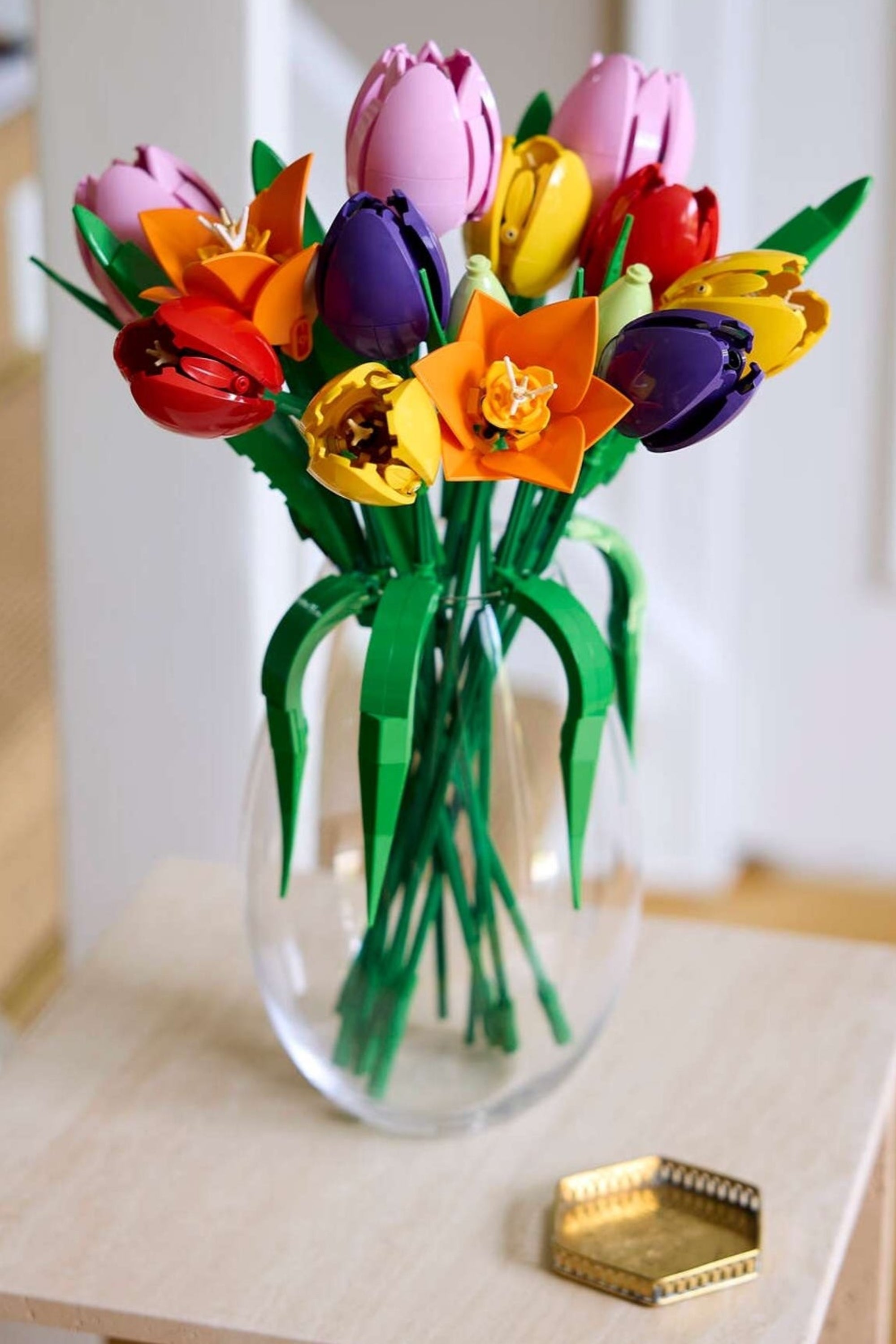 A vase of vibrant, multicolored LEGO flowers on a wooden stand near a staircase