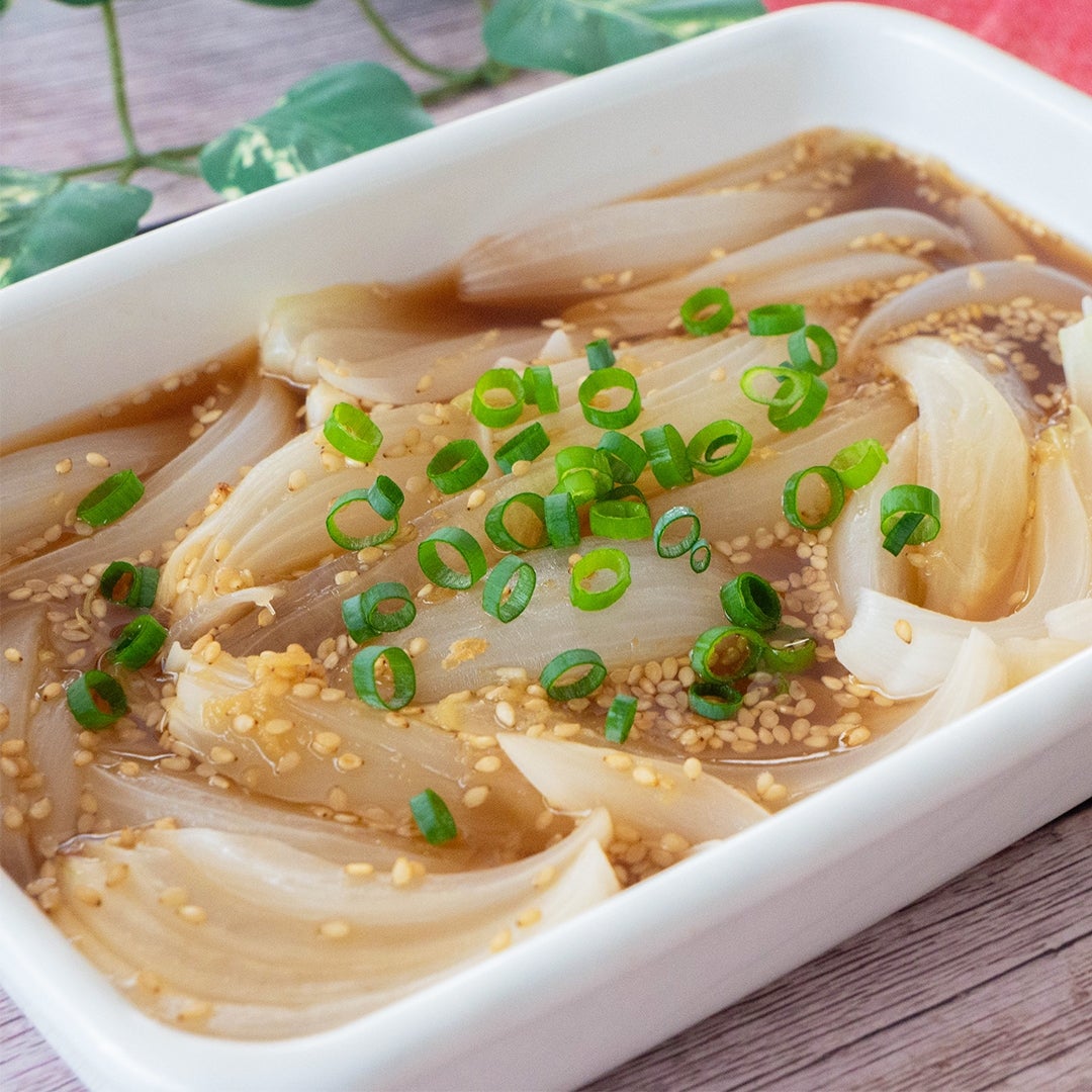 玉ねぎにタレがかけられ、ねぎとごまがトッピングされた料理が白い皿に盛られている。