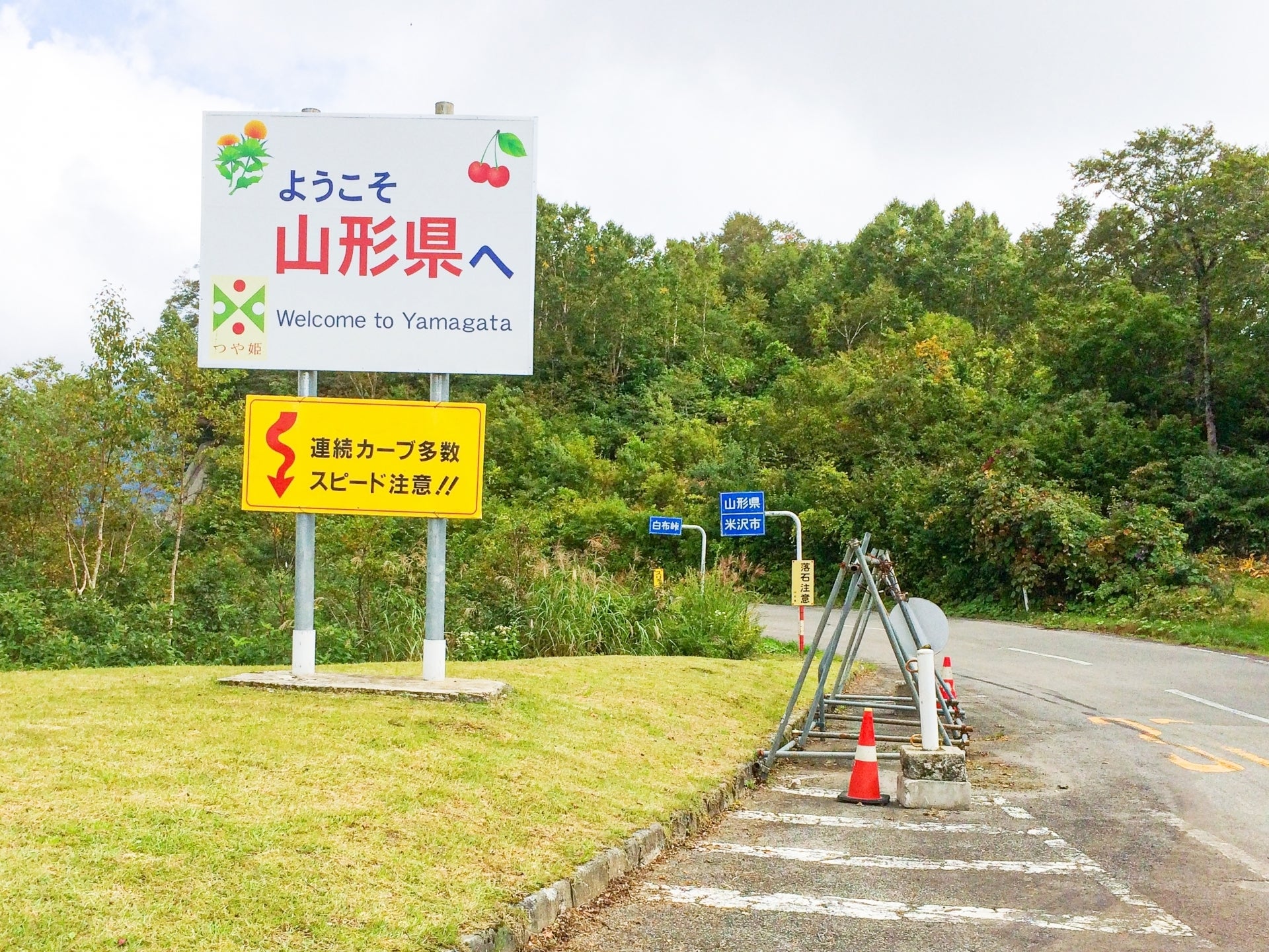 山形県へのようこそ看板。道路脇に注意を促す標識とオレンジのコーンが配置されています。