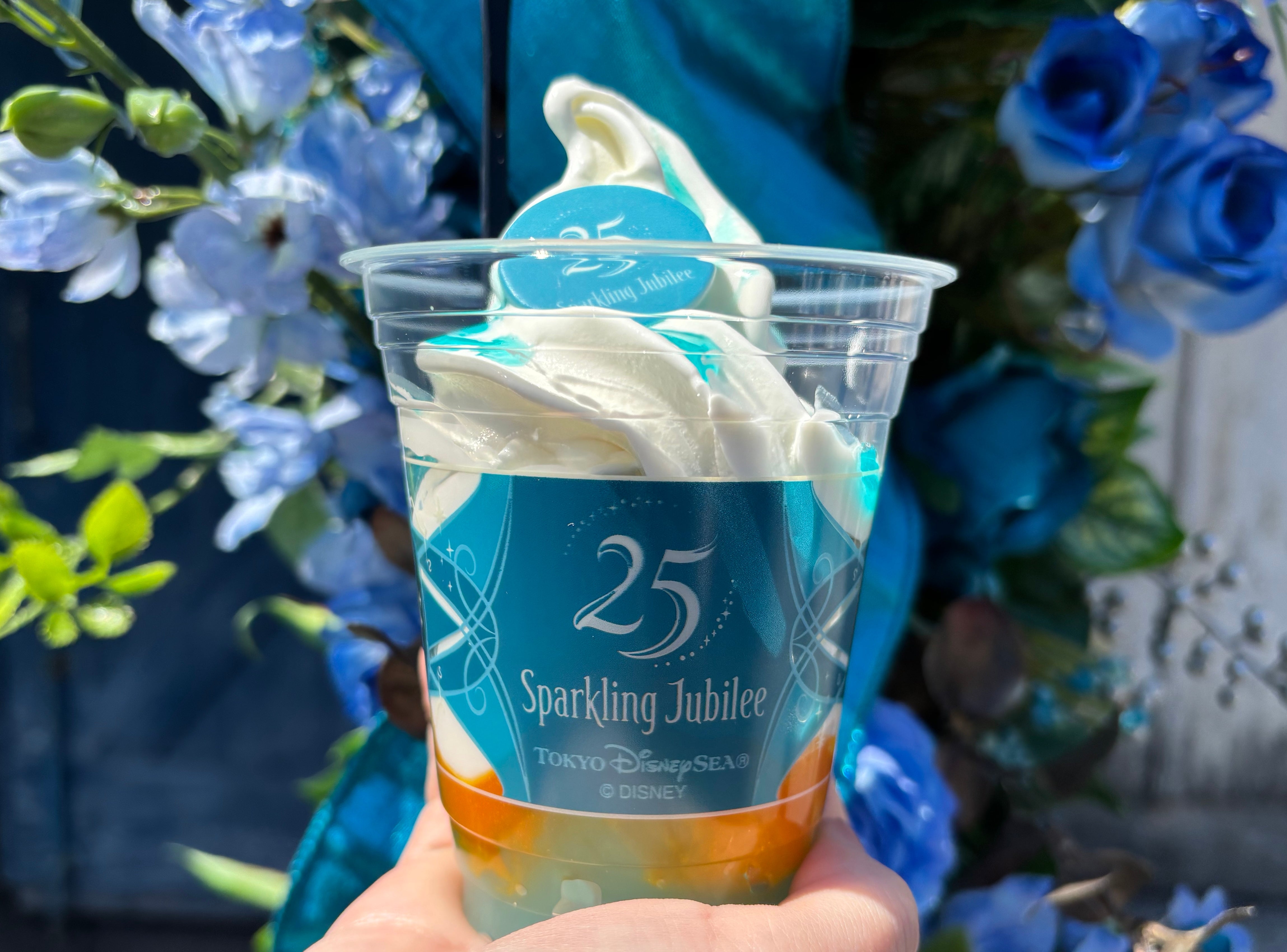 東京ディズニーシー25周年記念、ソフトクリームが載った限定デザートカップ。背景に青い花が飾られている。