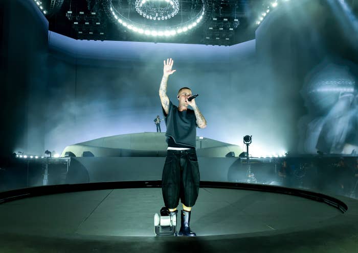 Performer connected  signifier    wearing escaped   pants and a sleeveless shirt, holding a microphone with 1  manus  raised, nether  melodramatic  lighting