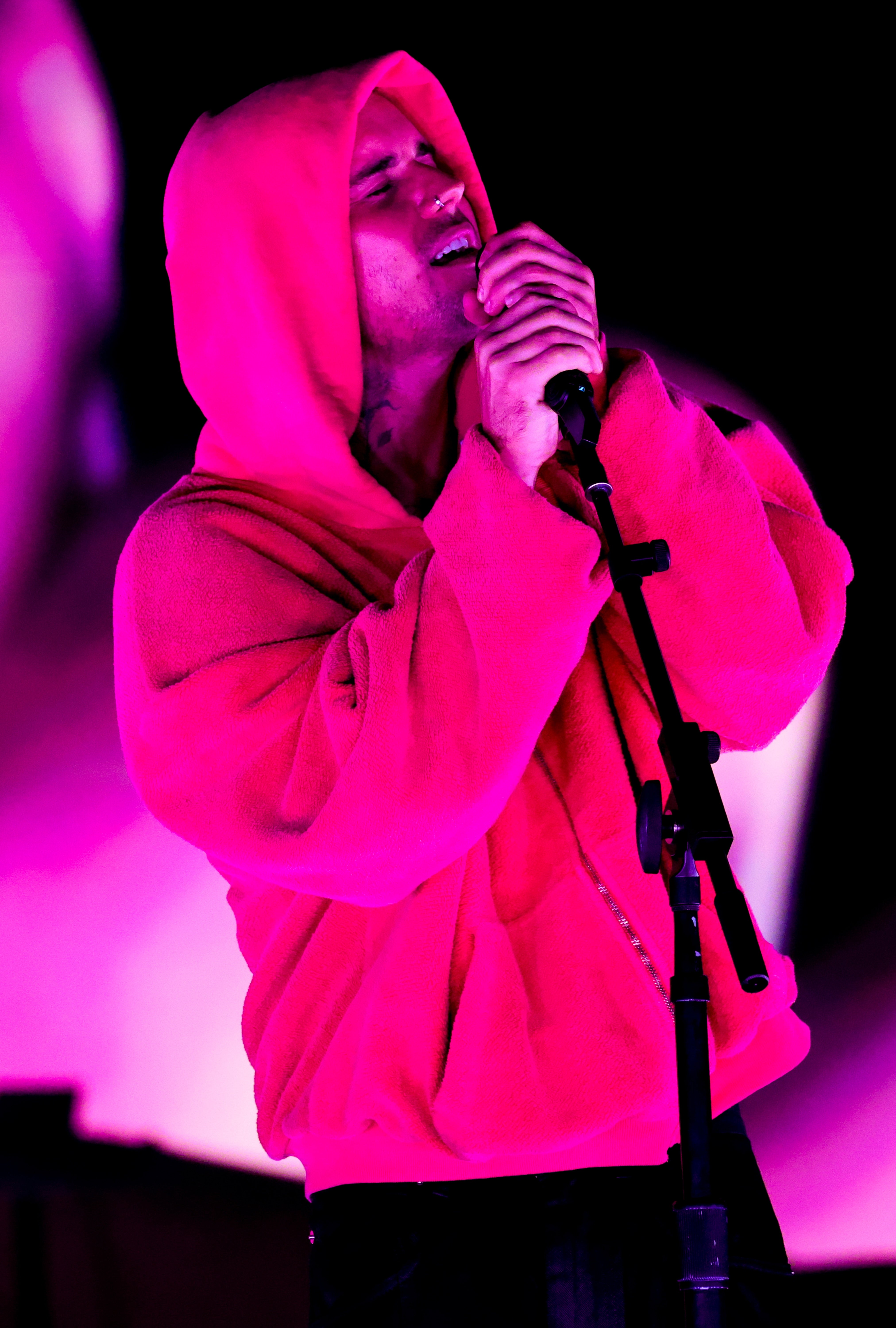 Person singing passionately connected stage, wearing an oversized hoodie, holding a microphone, with melodramatic lighting
