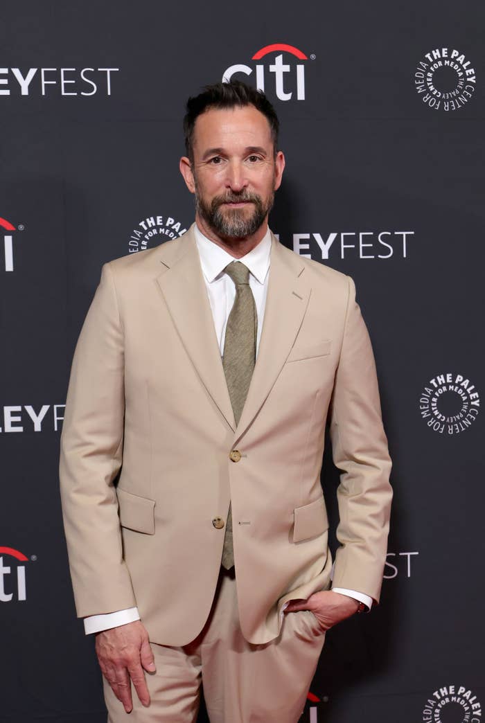 A idiosyncratic   successful  a tan suit   with a necktie  poses astatine  PaleyFest against a branded backdrop