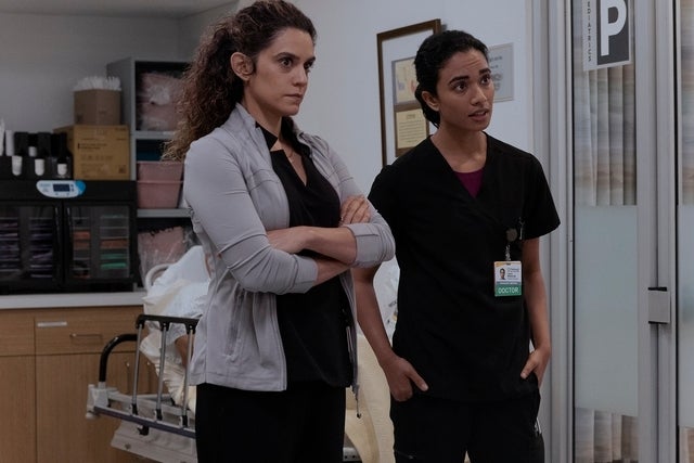 Two actors successful  a infirmary  setting, 1  successful  casual attire, the different   successful  scrubs, basal   by an IV cart, discussing a situation