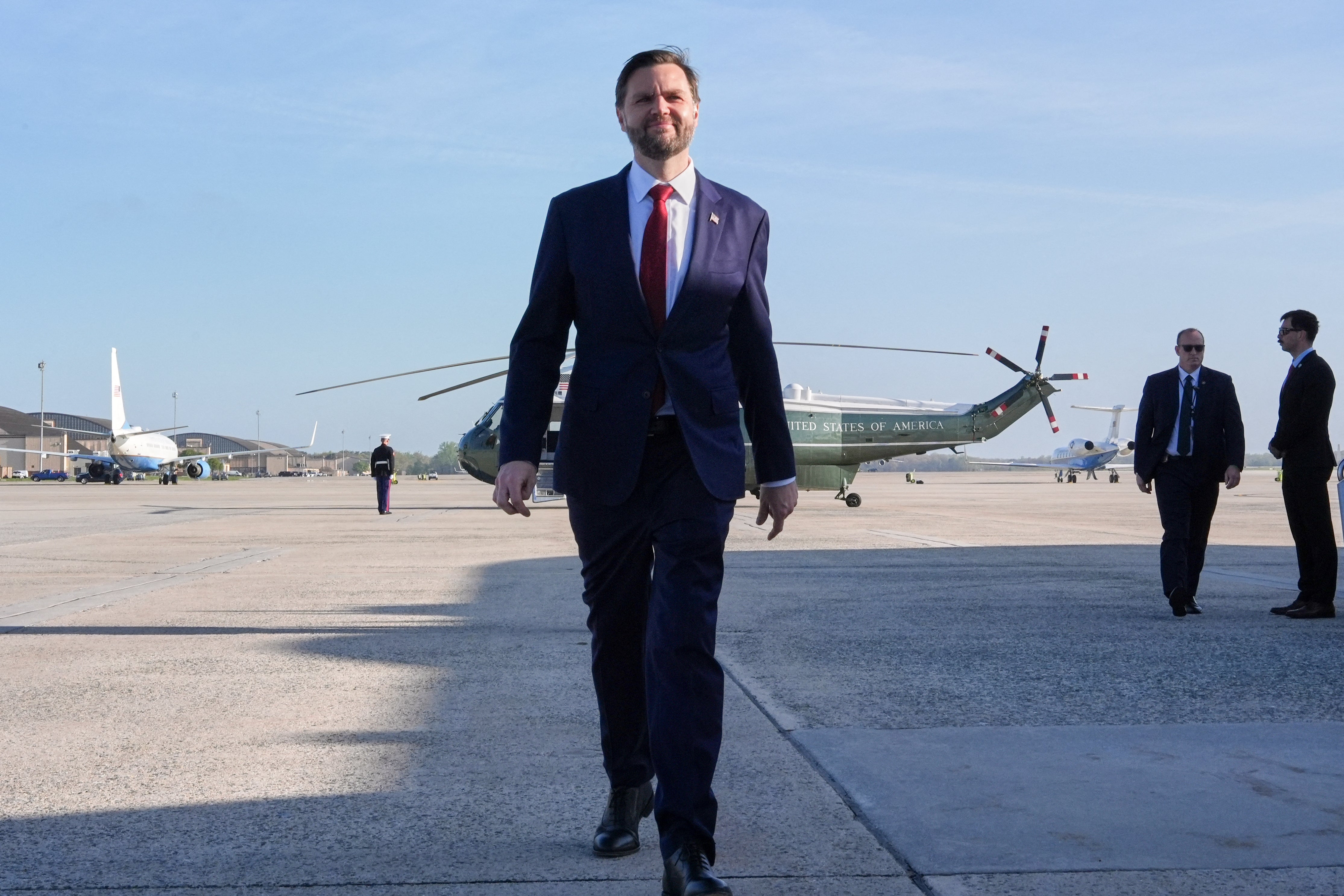 A antheral successful a suit and necktie walks confidently connected an airdrome tarmac, with helicopters and radical successful the background