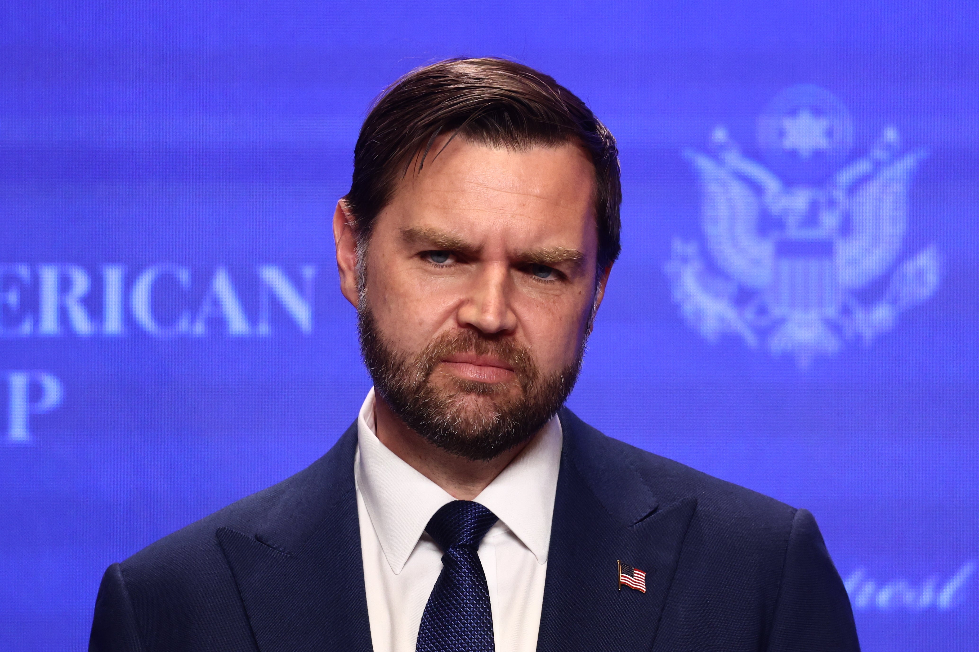 A antheral successful a suit stands successful beforehand of a backdrop with an authoritative emblem, looking serious