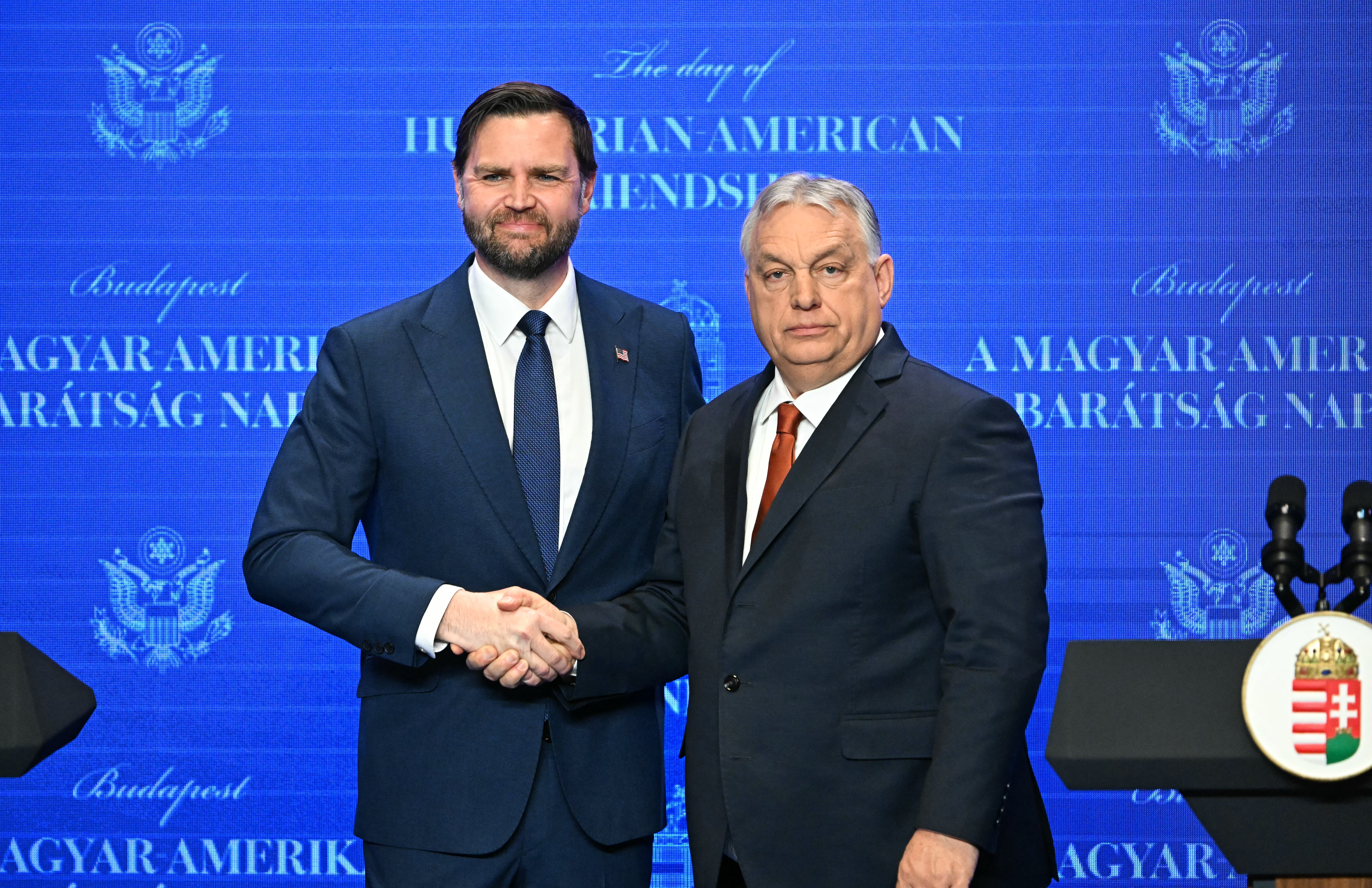 Two men successful suits shingle hands connected signifier successful beforehand of a surface speechmaking "Hungarian American Friendship."