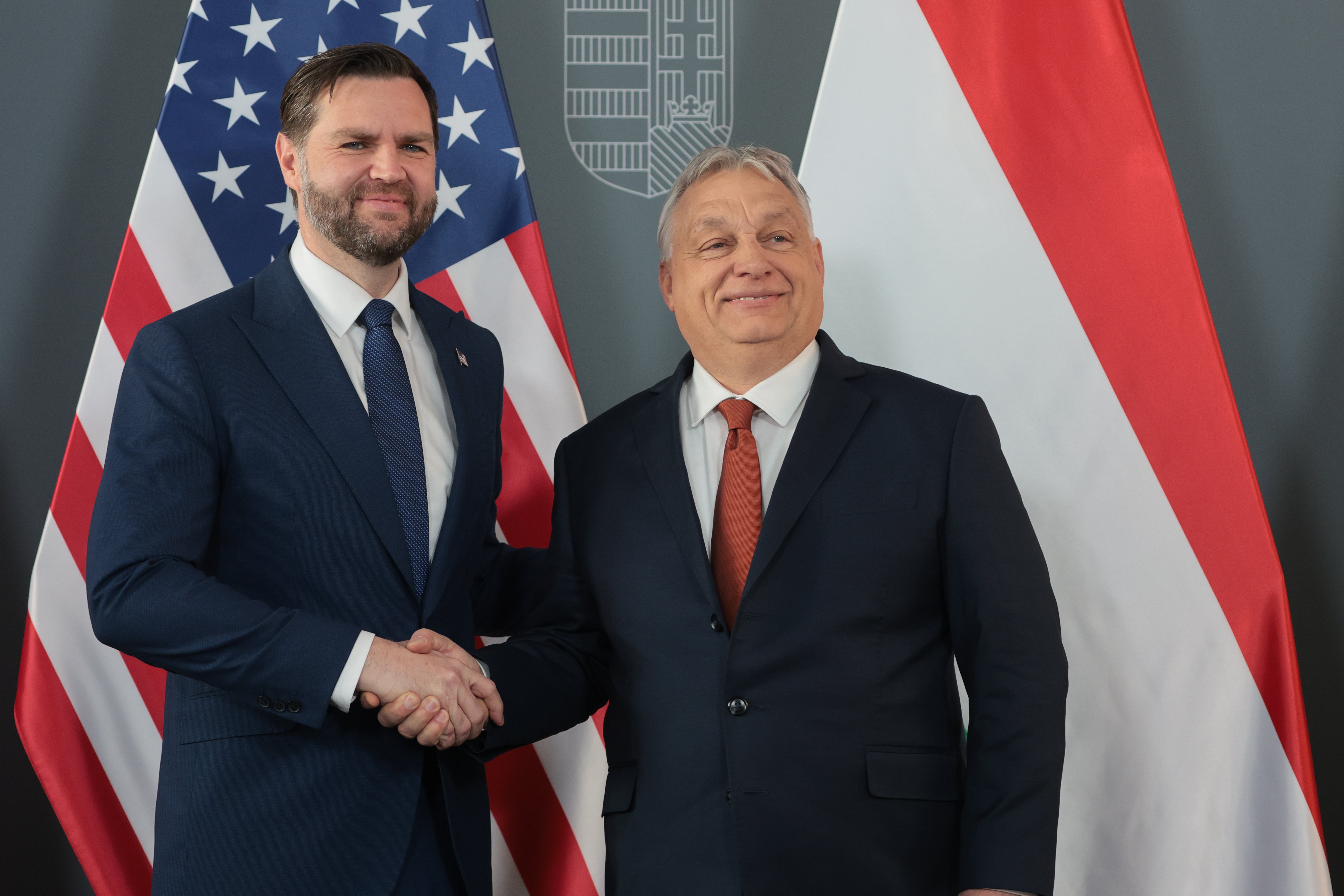 Two men successful suits shaking hands successful beforehand of American and Hungarian flags astatine a ceremonial event