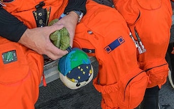 Two astronauts successful orangish suits beryllium wrong a helicopter, receiving instructions from a lasting idiosyncratic successful a bluish suit with NASA patches
