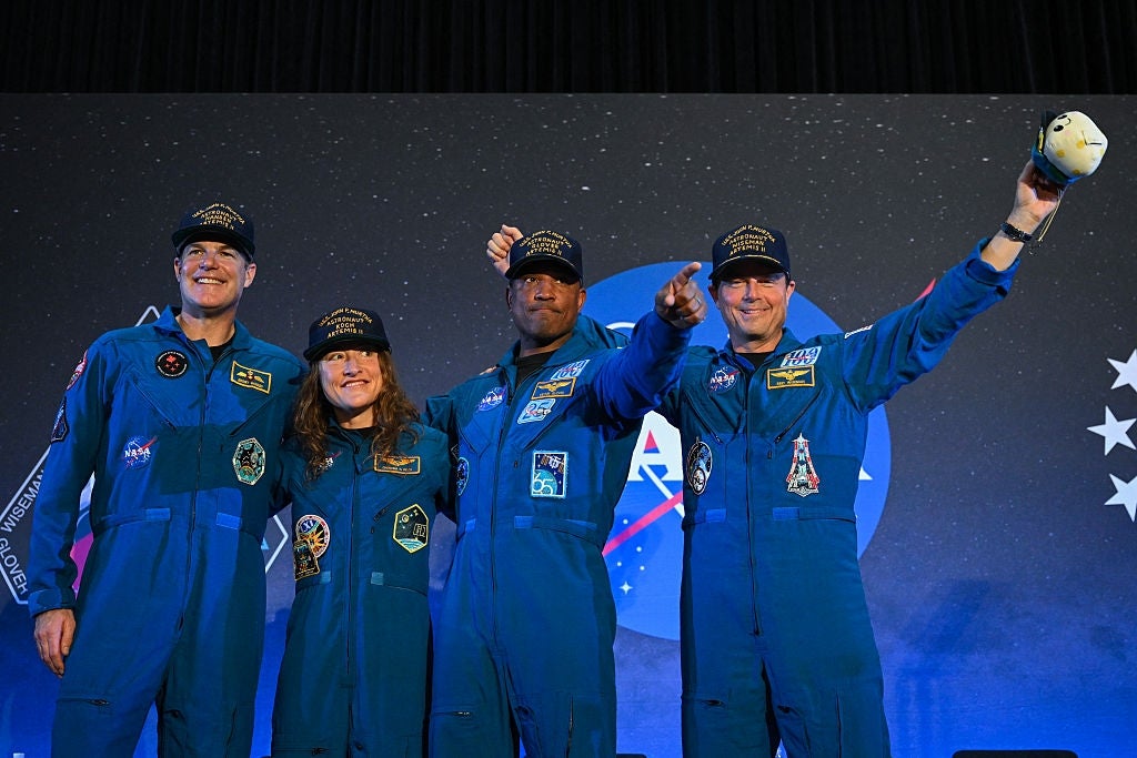 Four individuals successful bluish formation suits with ngo patches, posing proudly connected stage, 2 pointing forward, each wearing caps