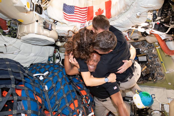 Four astronauts successful  a abstraction  module clasp  each   other, smiling, surrounded by instrumentality  with U.S. and Canadian flags visible