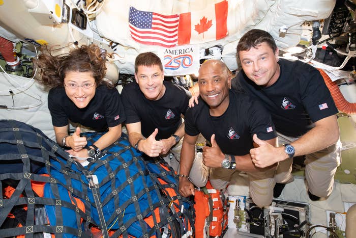 Four astronauts floating successful  a spacecraft, each  giving thumbs up. U.S. and Canadian flags visible. They deterioration  matching ngo  shirts