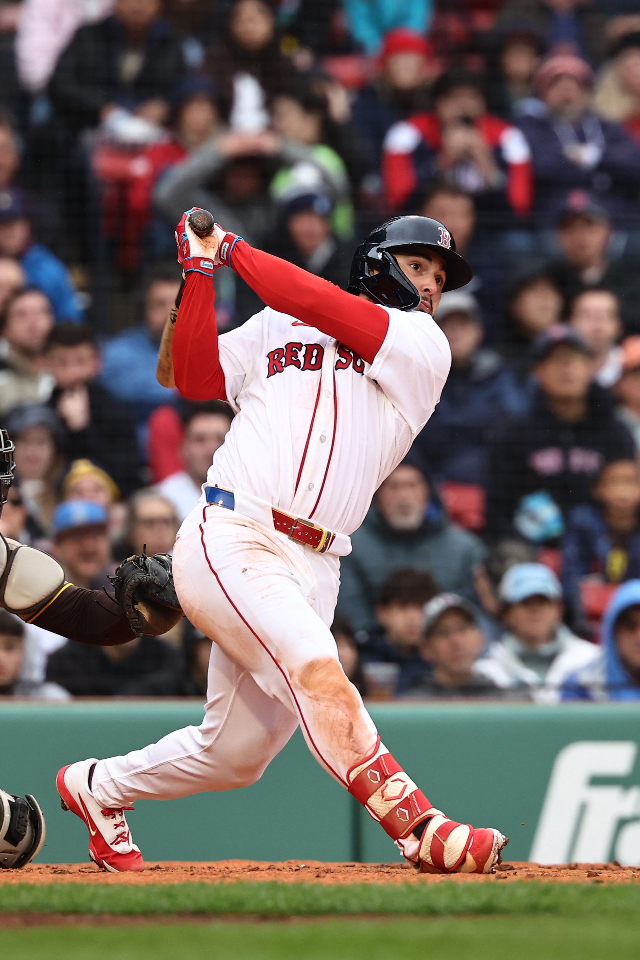 Baseball subordinate    swings bat vigorously during a game, wearing a helmet and achromatic  azygous   with "Red Sox" connected  the front. Crowd watches successful  background