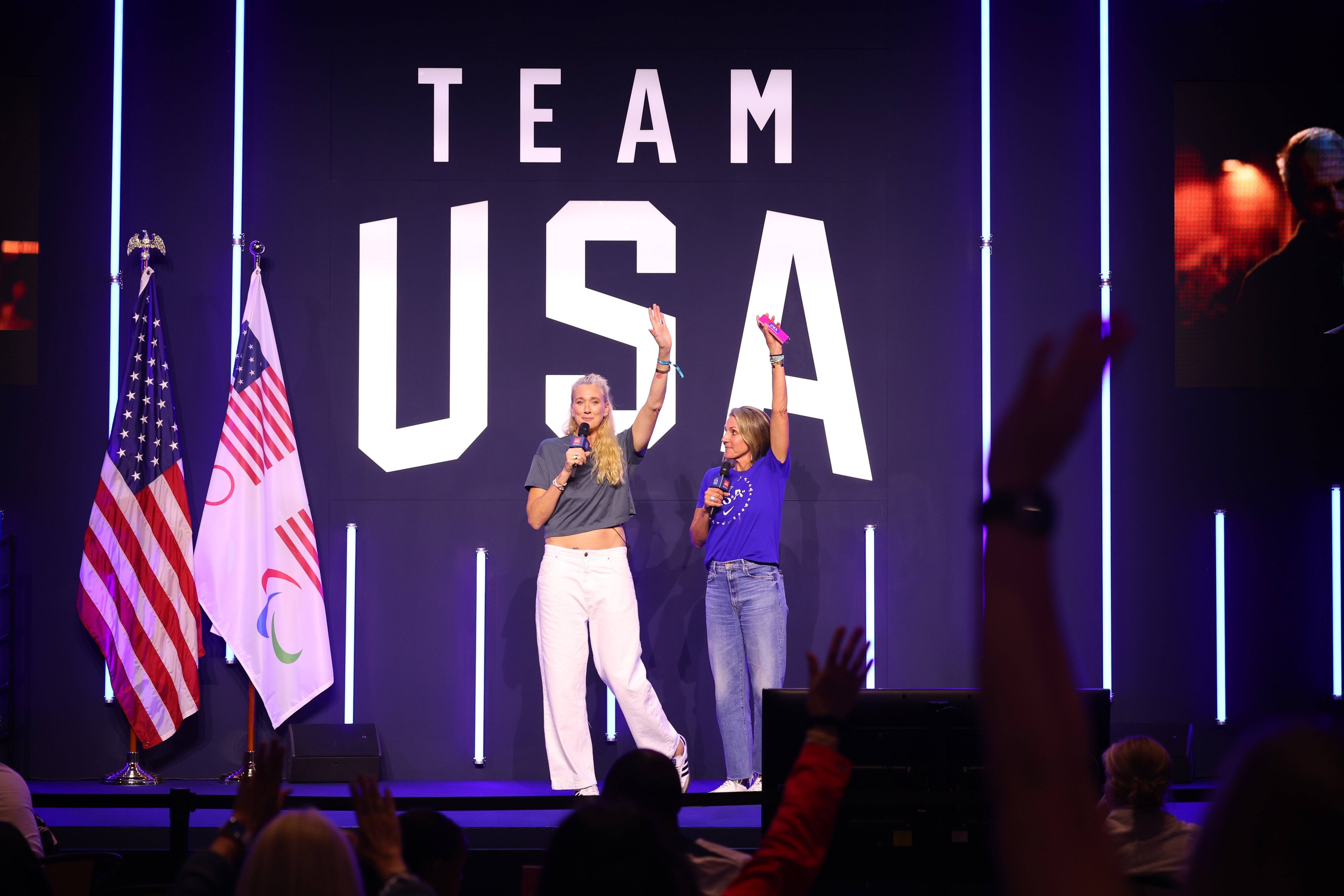 Two radical   connected  signifier    astatine  a Team USA event, holding microphones, rise  hands successful  celebration. Audience members' hands are seen successful  the foreground