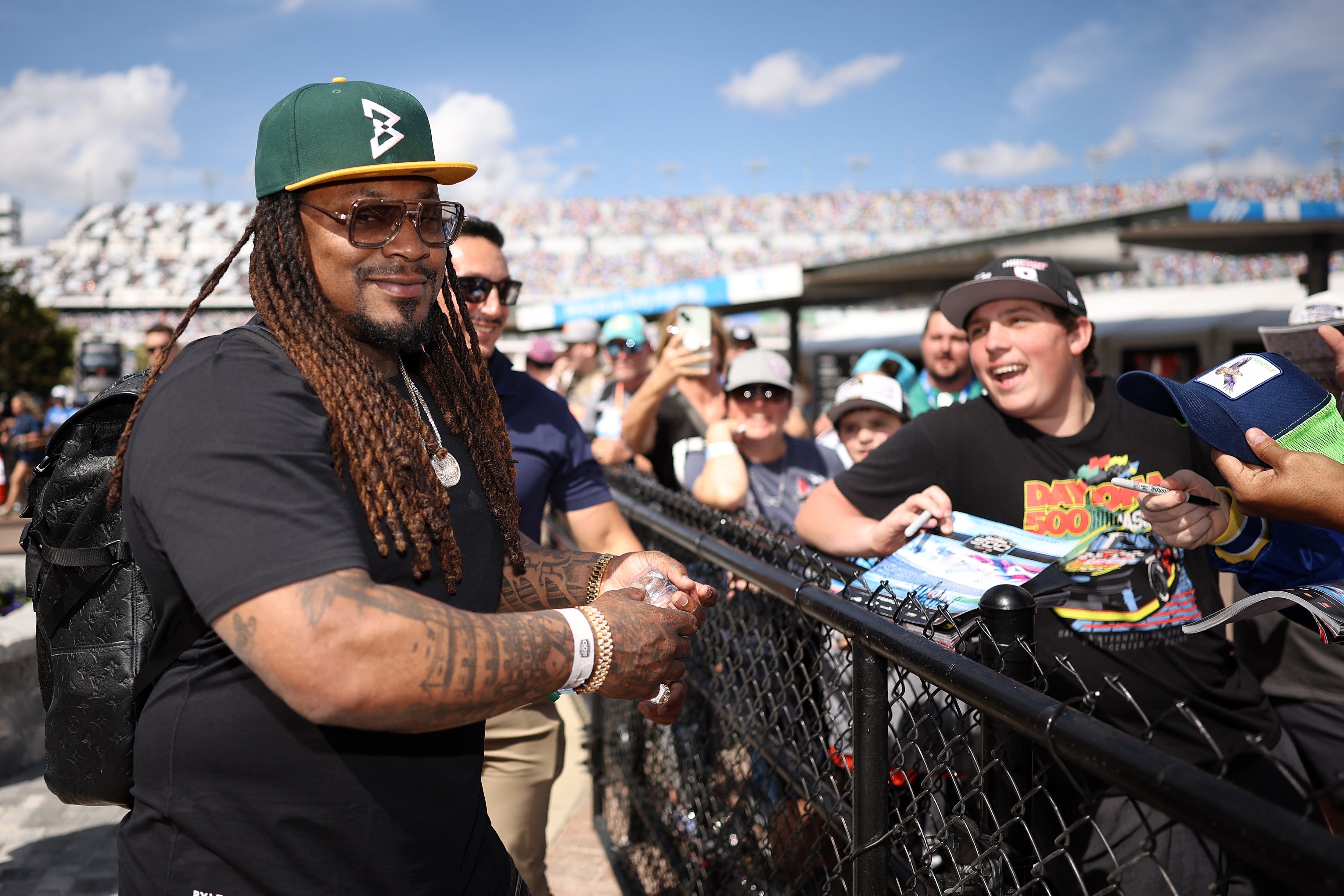 Person with agelong  hairsbreadth  and sunglasses, wearing a headdress  and casual clothing, signing autographs for enthusiastic fans astatine  an outdoor event