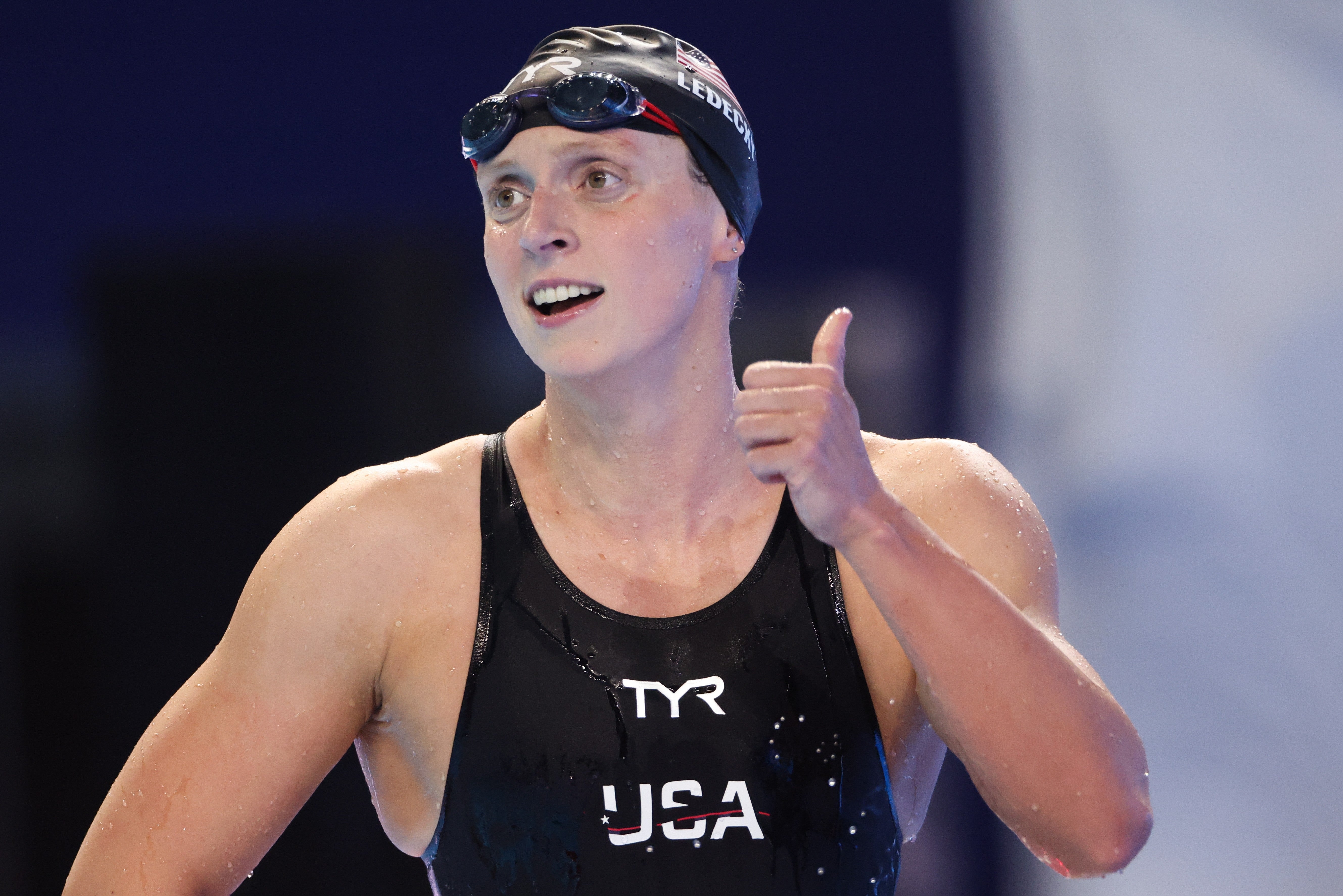 An jock  successful  a aquatics  headdress  and goggles smiles and gives a thumbs up   aft  a aquatics  competition. "USA" and "TYR" are disposable   connected  the swimsuit